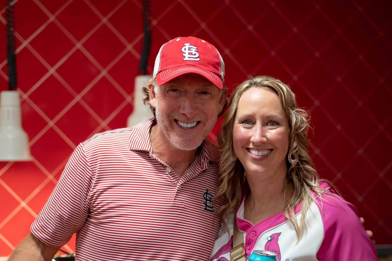 Two people wearing casual attire pose together, one in a red St. Louis Cardinals baseball cap and striped shirt.