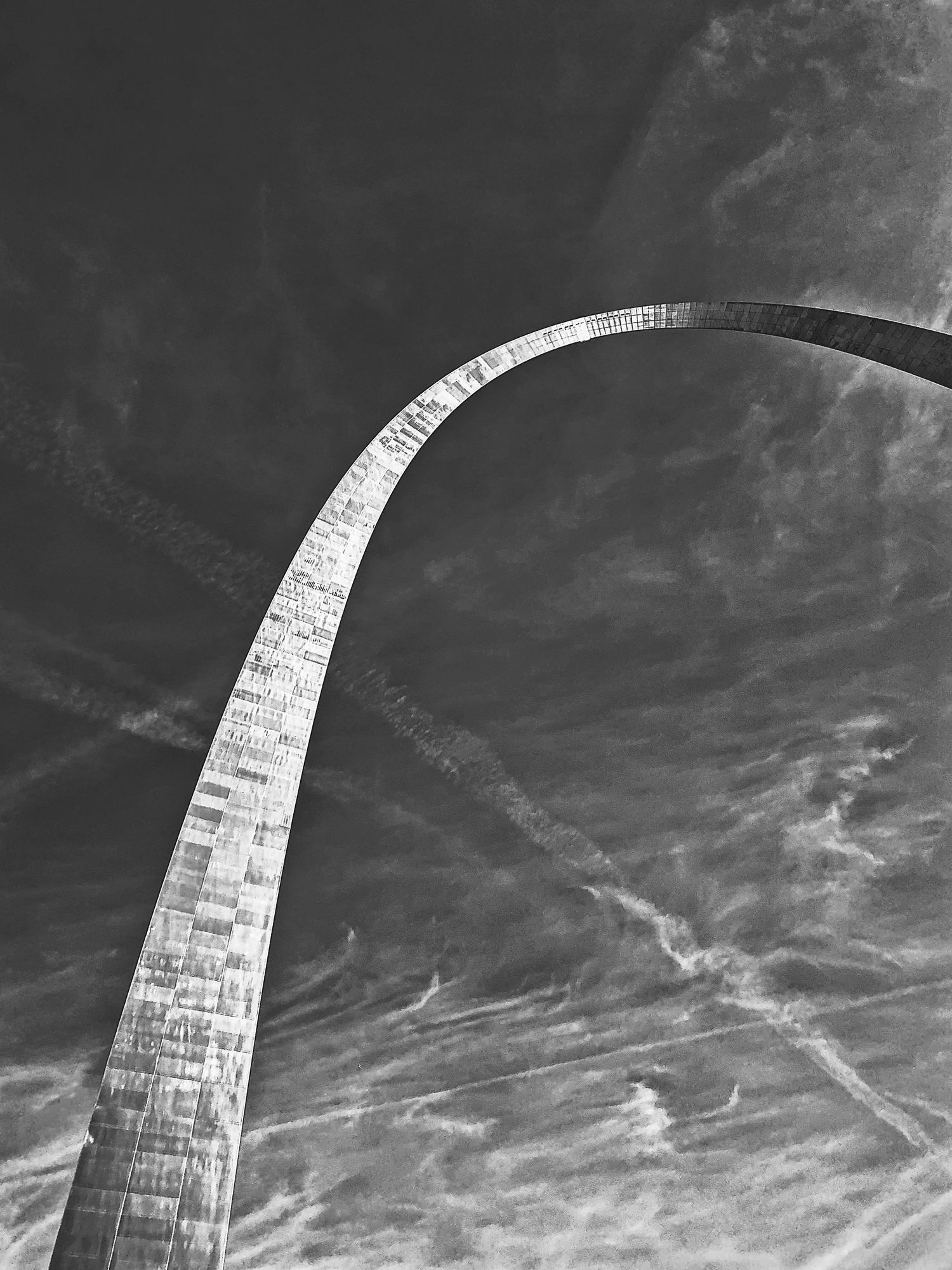 Curved architectural structure captured in black and white against cloudy sky.