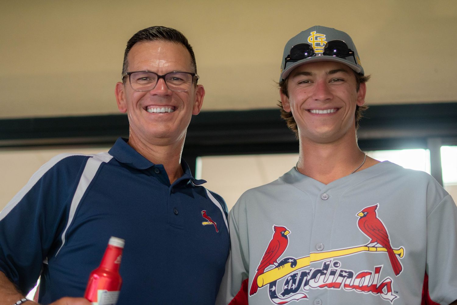 A group wearing Cardinals baseball jerseys and hats smiling together at what appears to be a stadium venue.
