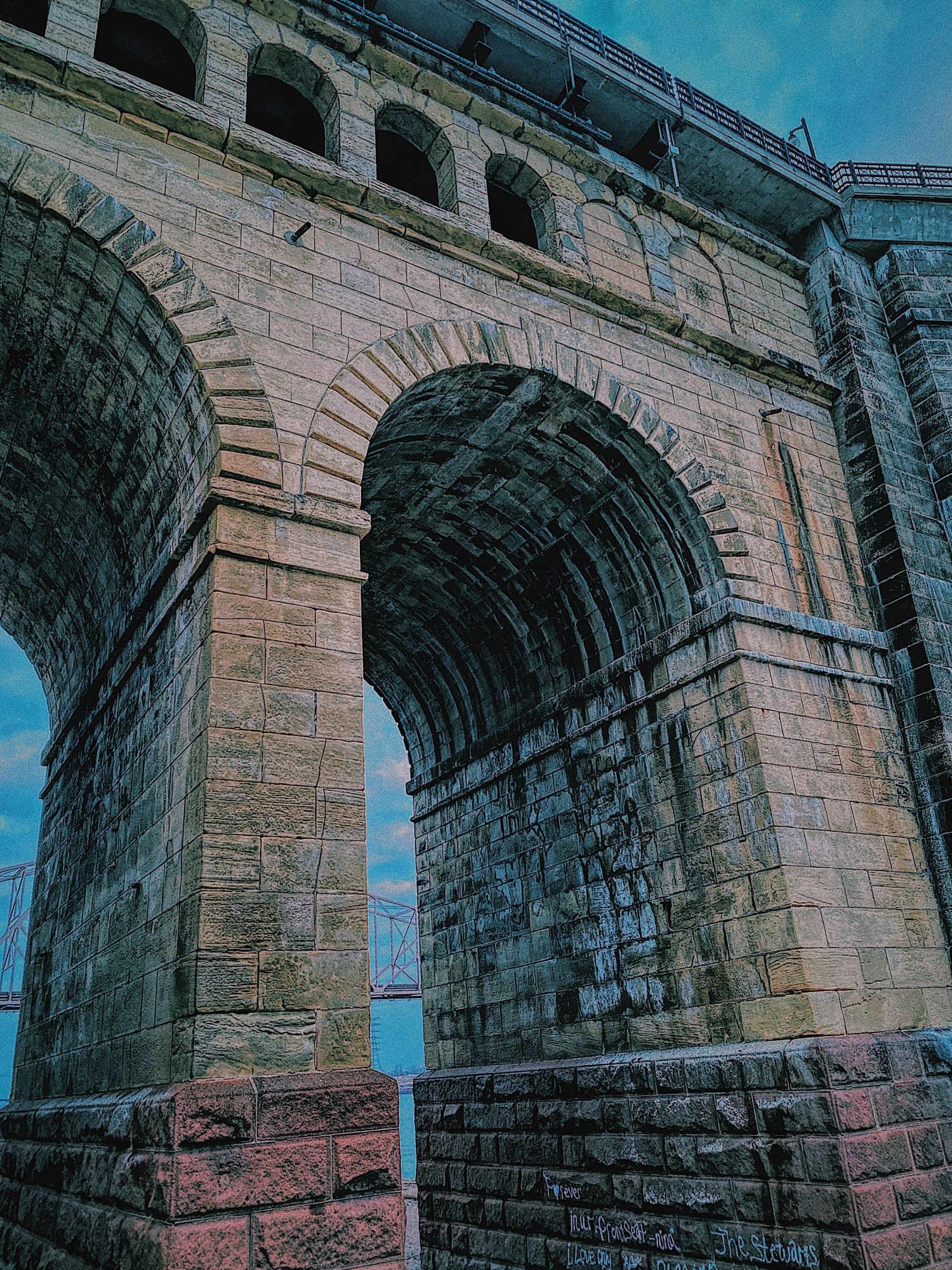 Ancient stone viaduct with multiple arches photographed against bright blue sky.