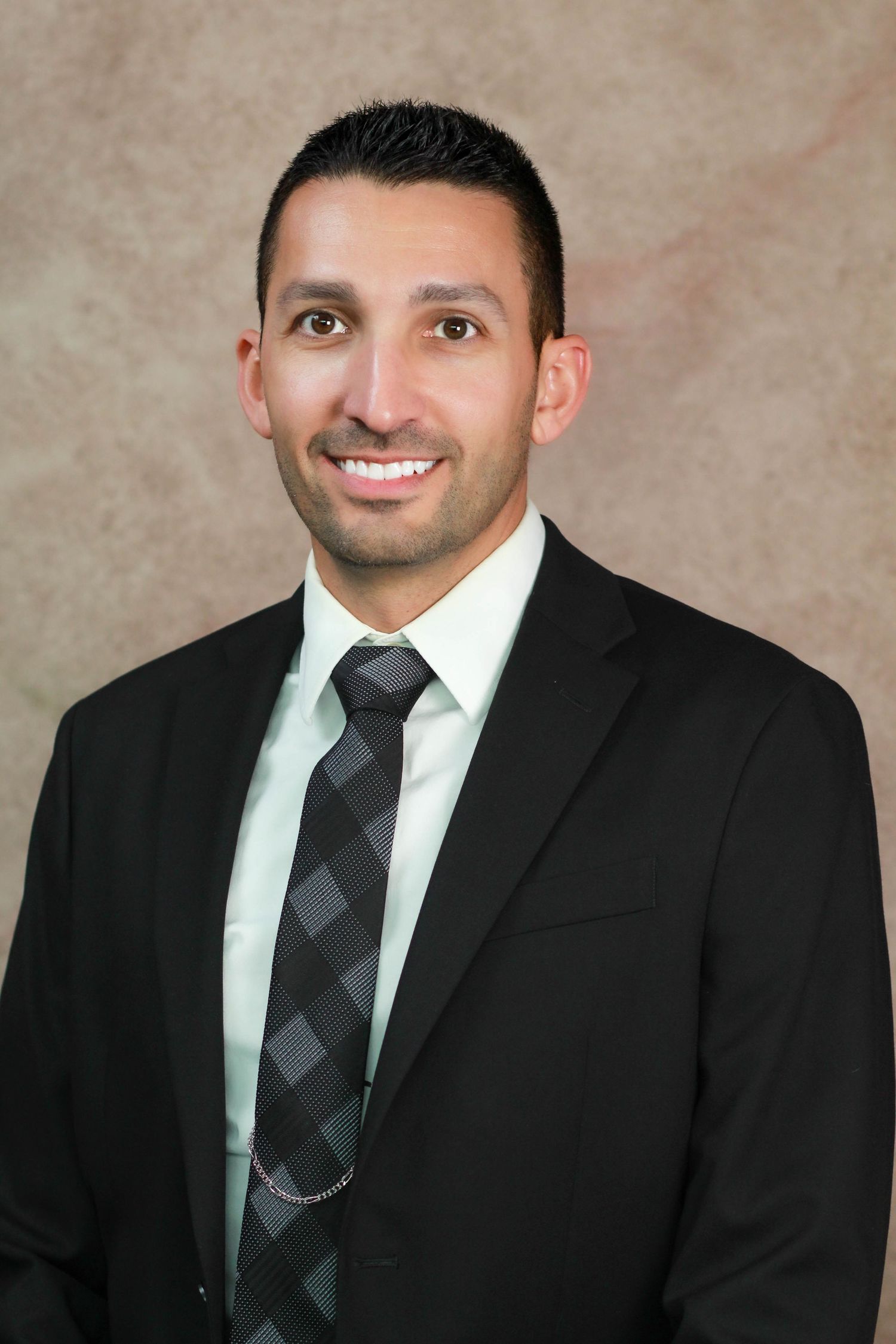 Professional headshot of person in dark suit with diagonal striped tie against neutral background.