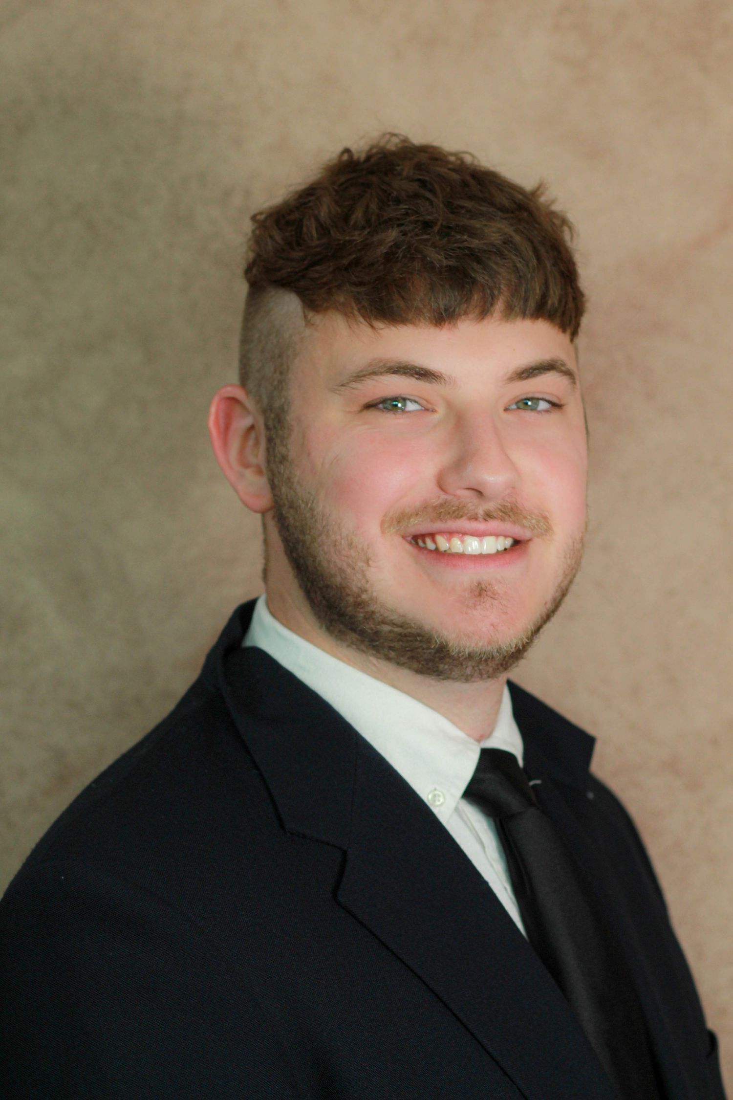 Professional headshot showing a smartly dressed young professional in a black suit and bowtie.