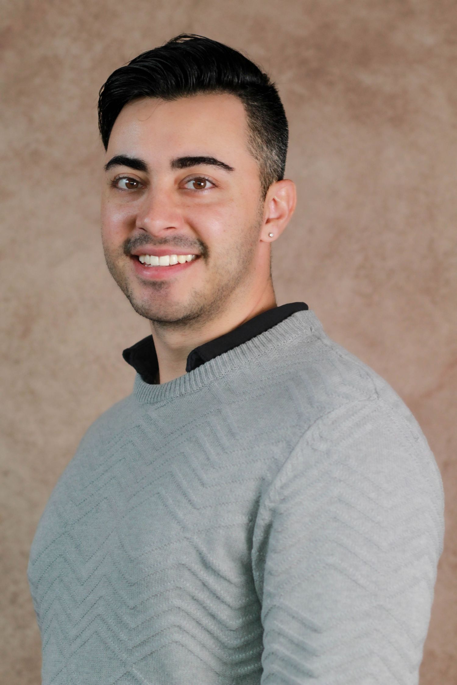 Person in grey textured sweater smiling warmly against neutral studio background.