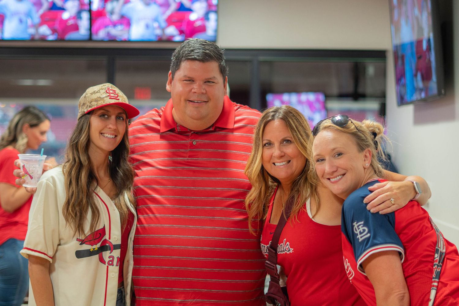 A group of baseball fans wearing Cardinals and Rangers jerseys pose together for a photo at a game.