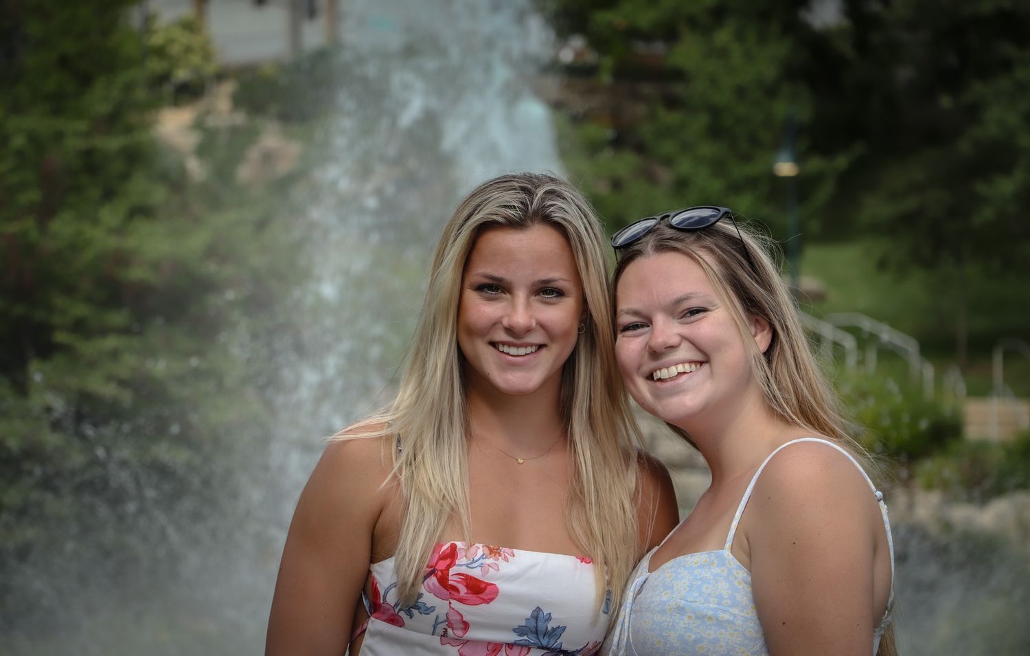 Two women share a joyful moment together in front of a cascading water fountain.