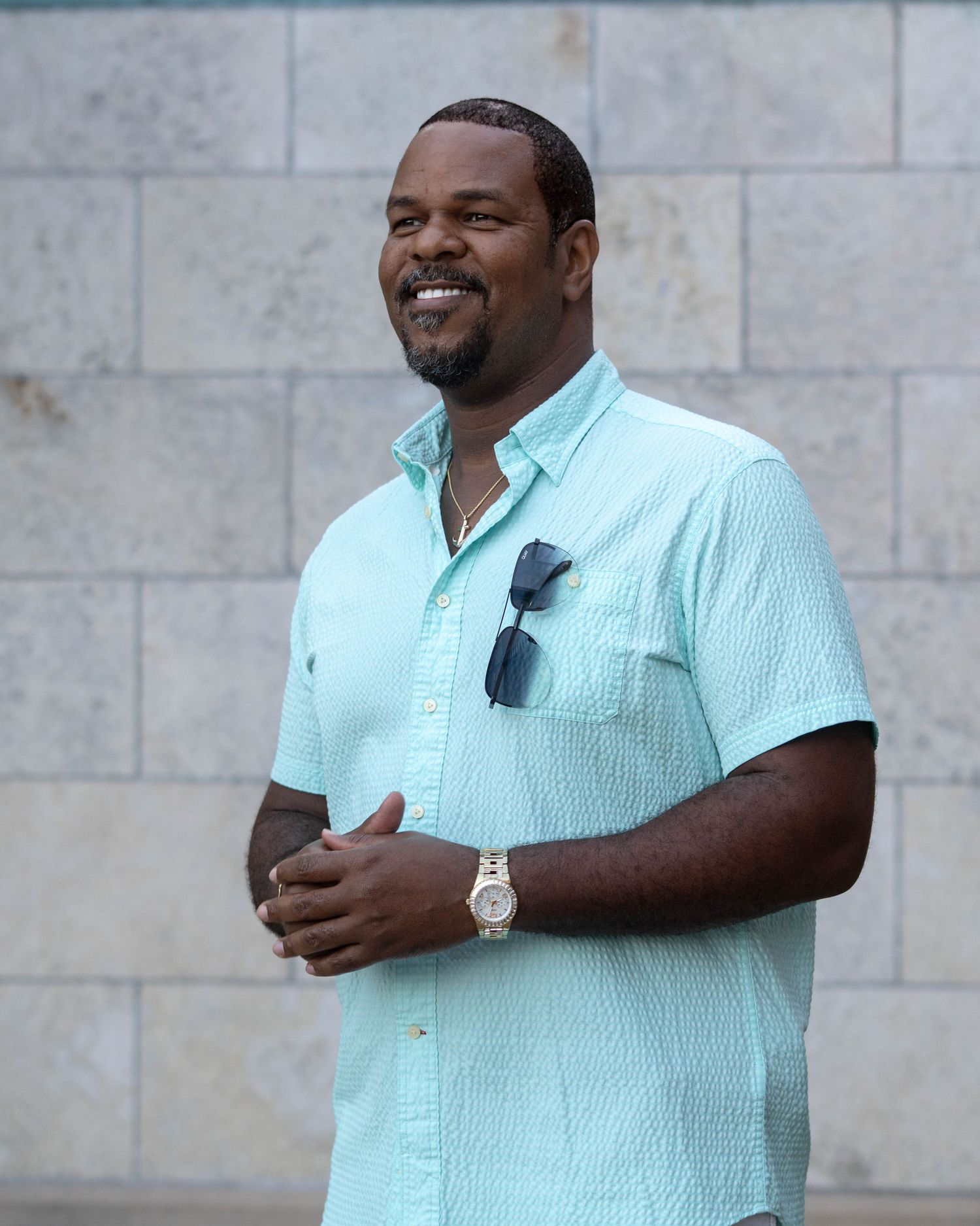 Casual portrait series of someone in light blue shirt smiling against stone wall background.