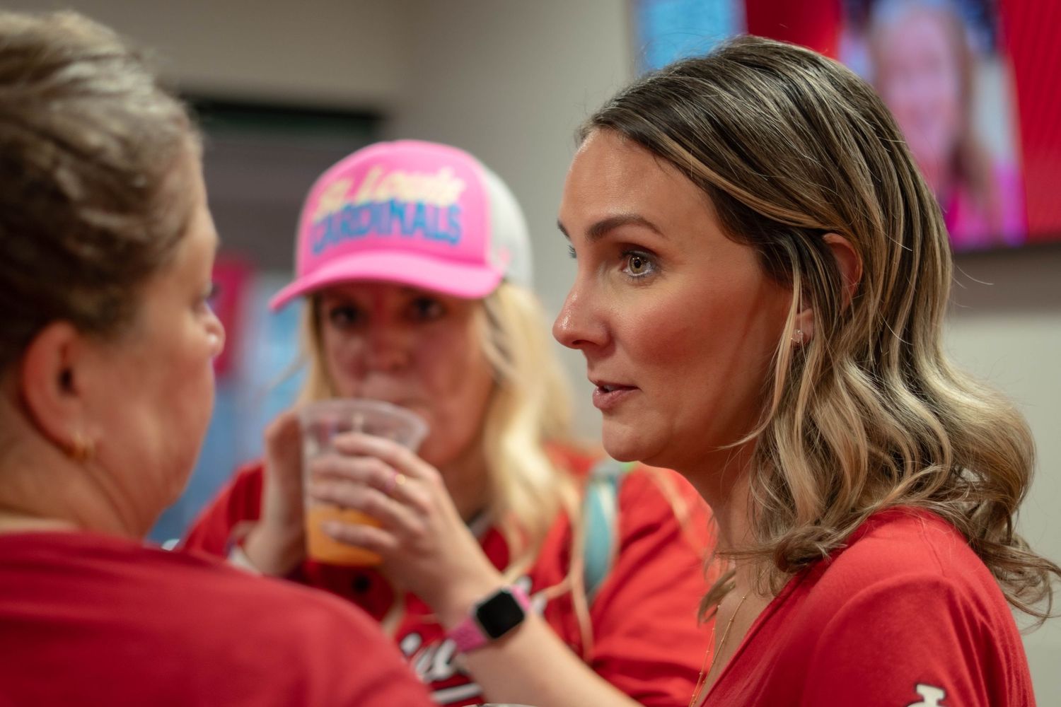 Baseball fans wearing red team jerseys watch a game from stadium seats while enjoying beverages.