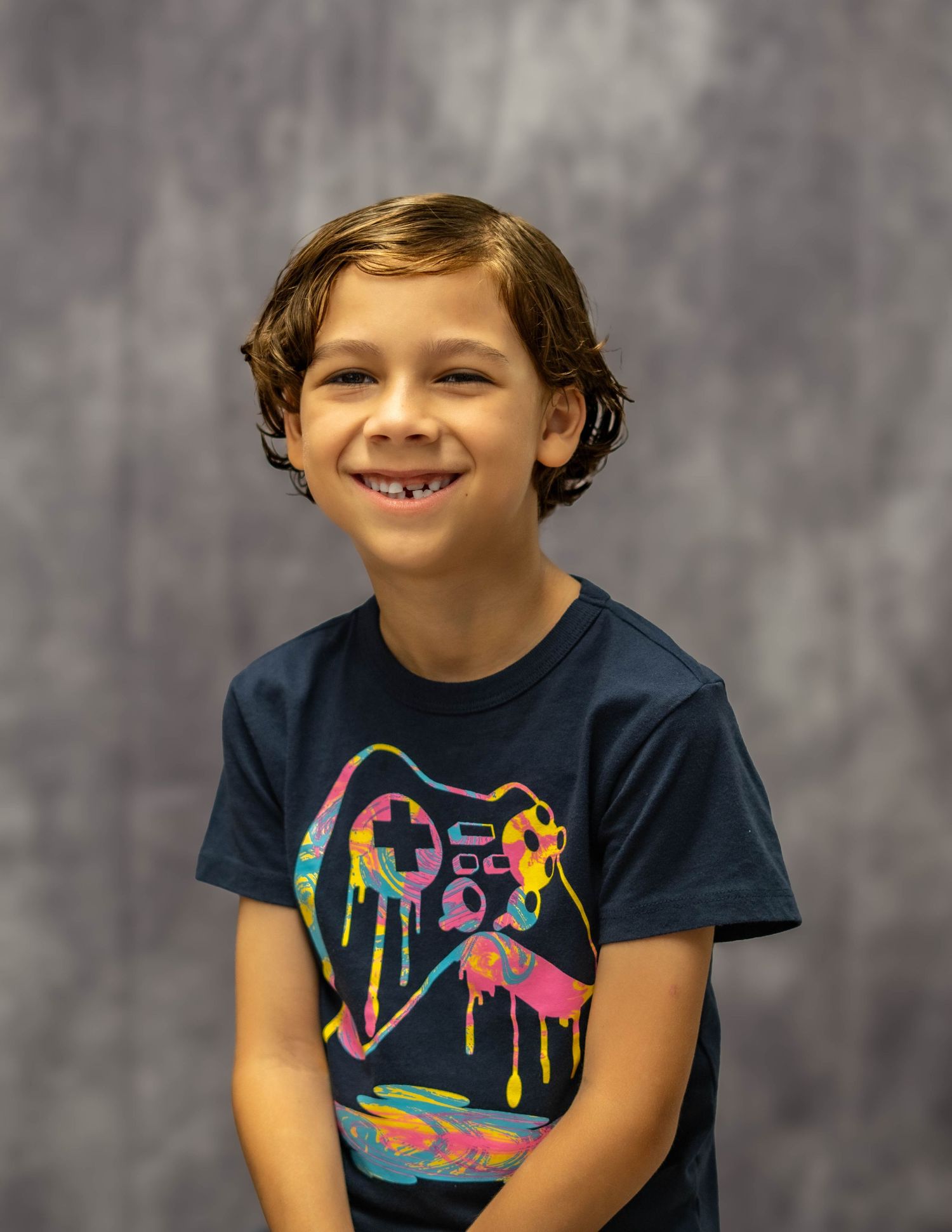 Young person wearing navy blue t-shirt with colorful graphic design smiling at camera against gray backdrop.