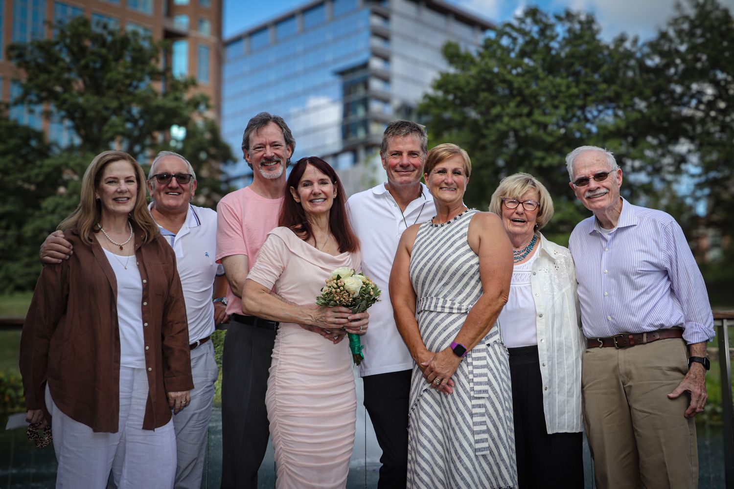 A group of smartly dressed people gather for a celebratory photo outdoors near a modern building.