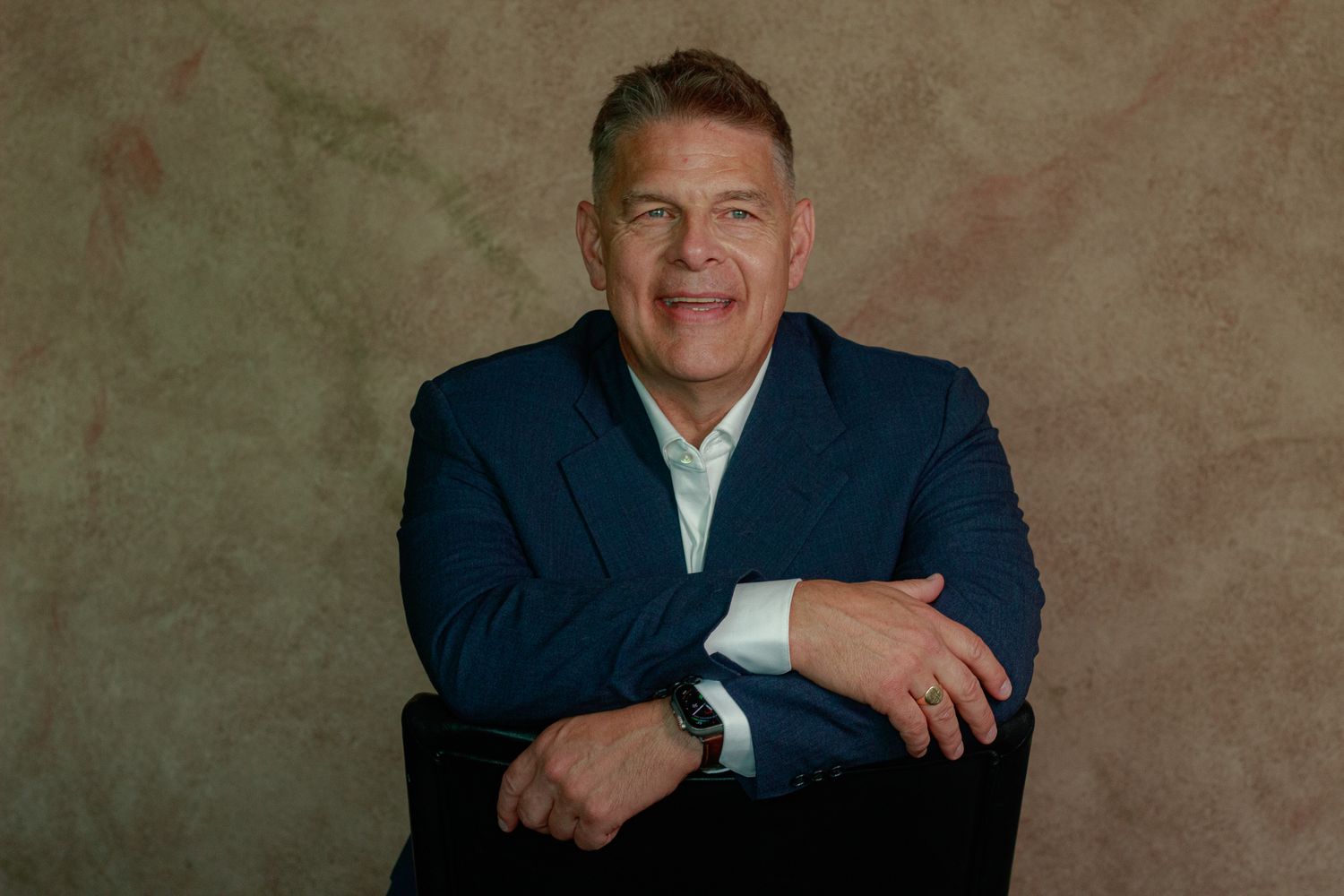 Business portrait of a professional in navy suit with relaxed pose against textured background.