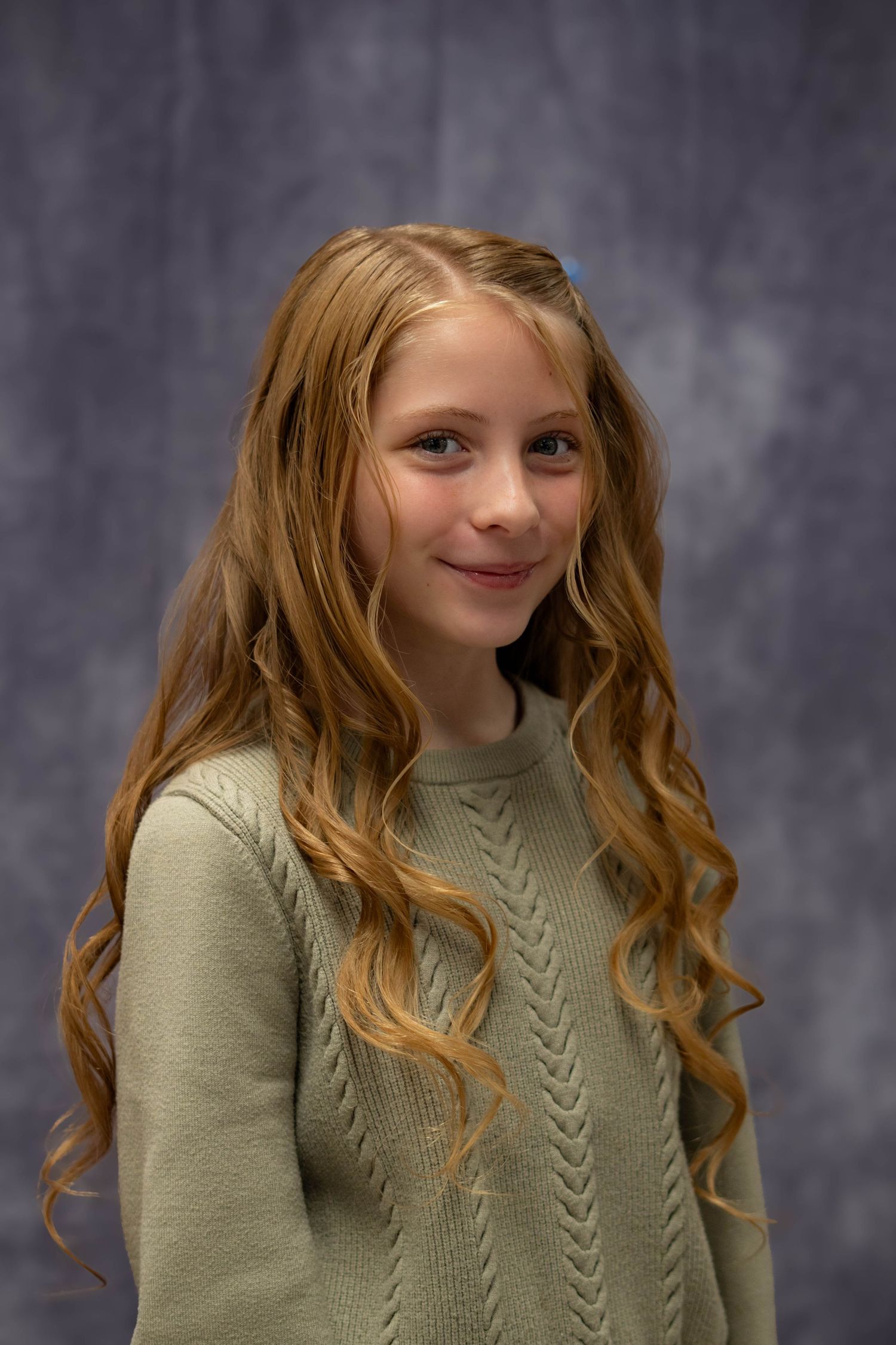 A series of four headshots showing someone with long wavy red hair wearing a sage green sweater against a gray backdrop.