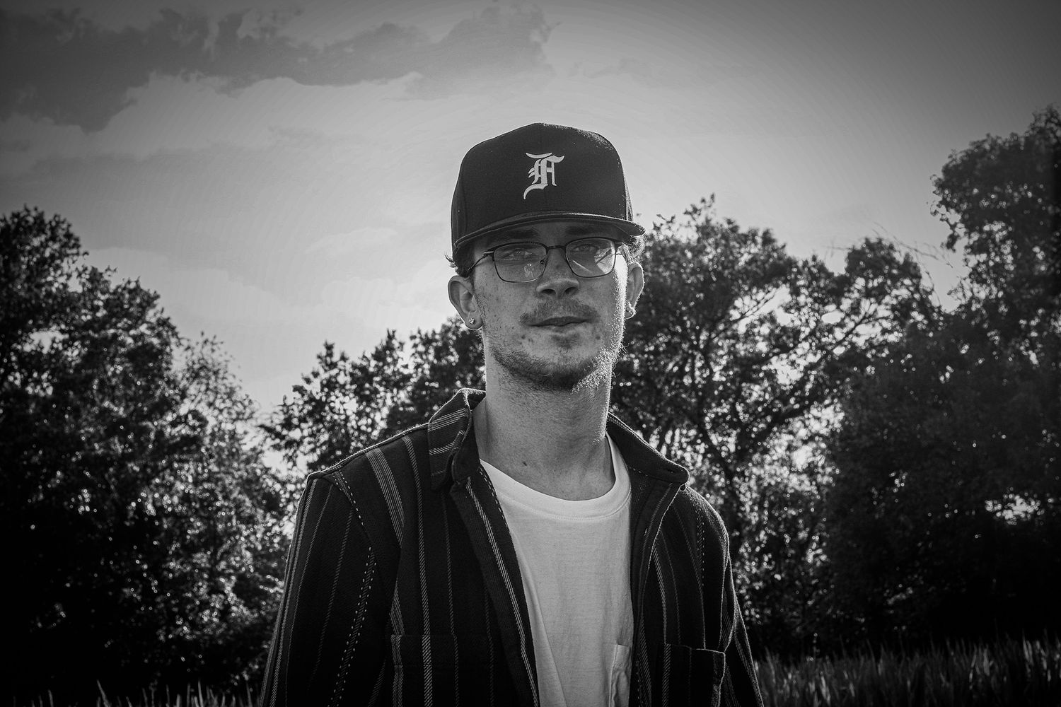 A series of seven black and white portraits showing a person wearing a baseball cap in various poses outdoors.