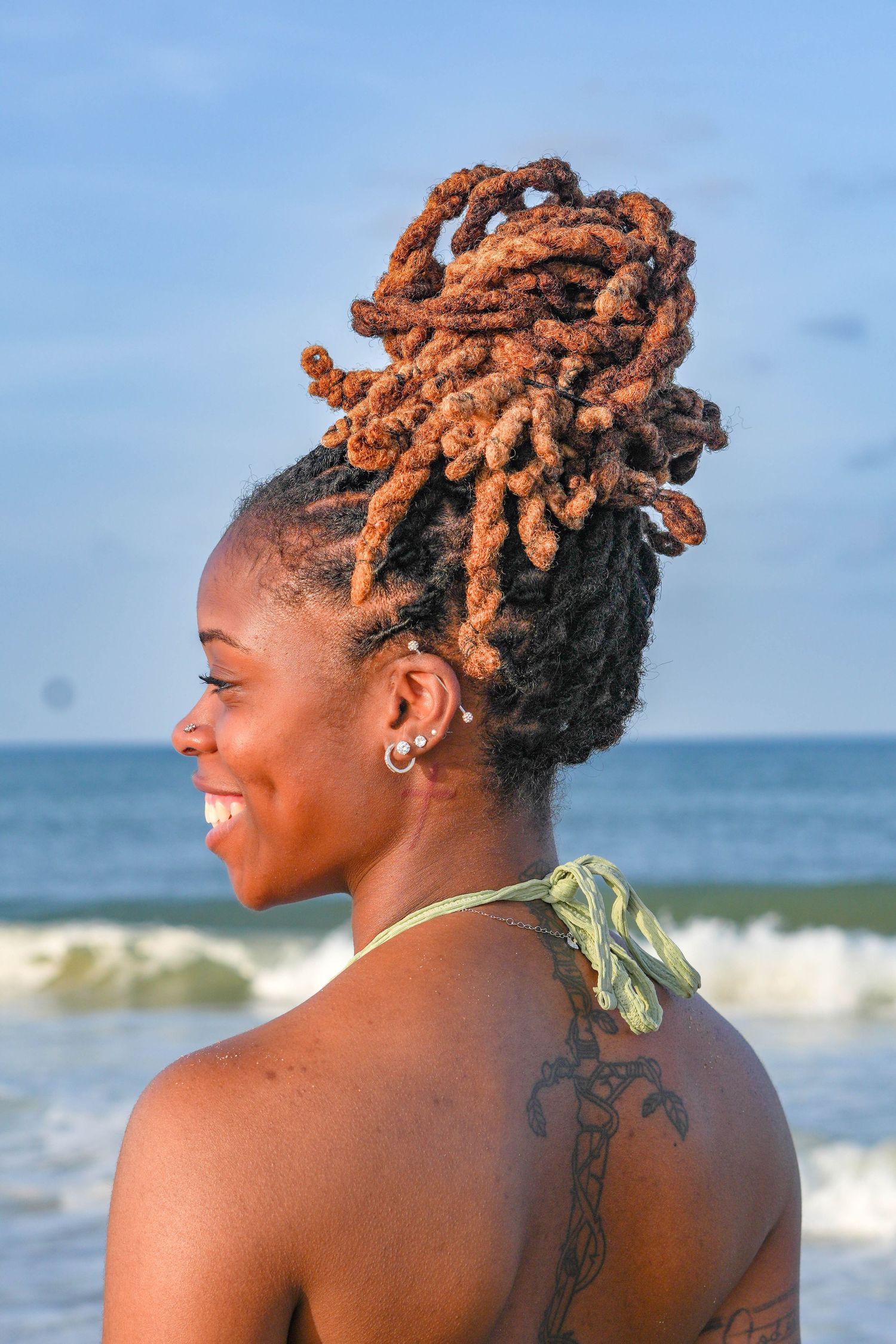 Profile view of someone with orange-tinted locs hairstyle enjoying a beach day.