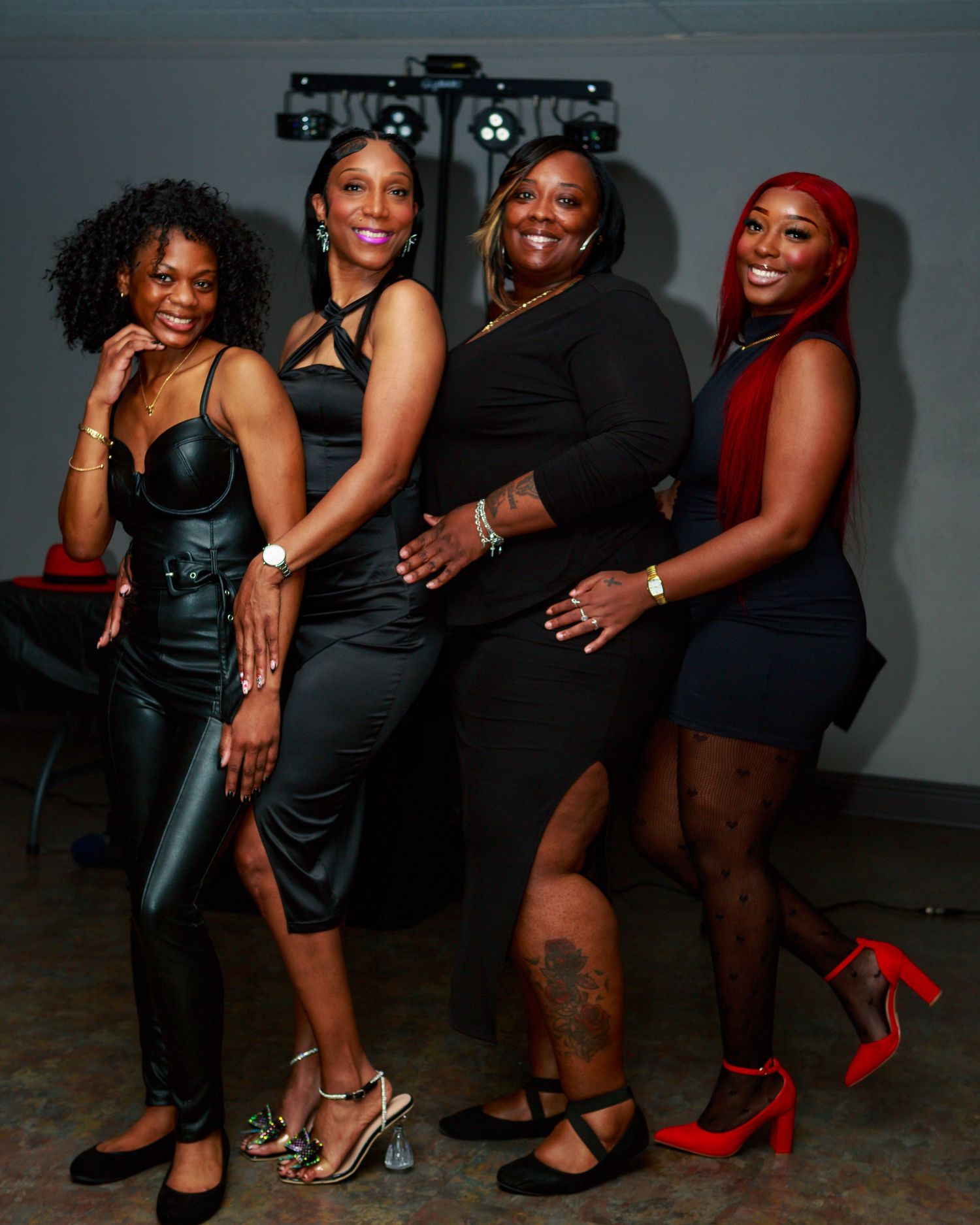 Four women in black outfits smile and pose together at an indoor evening celebration or party event.