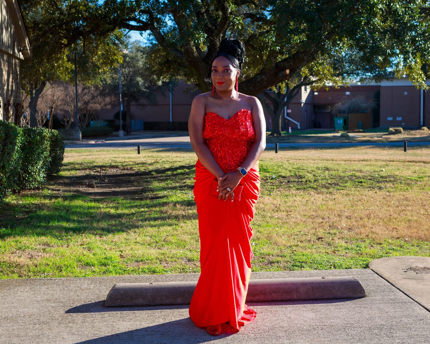 Young woman in elegant red sequin gown posing outdoors on sidewalk for formal event photo.