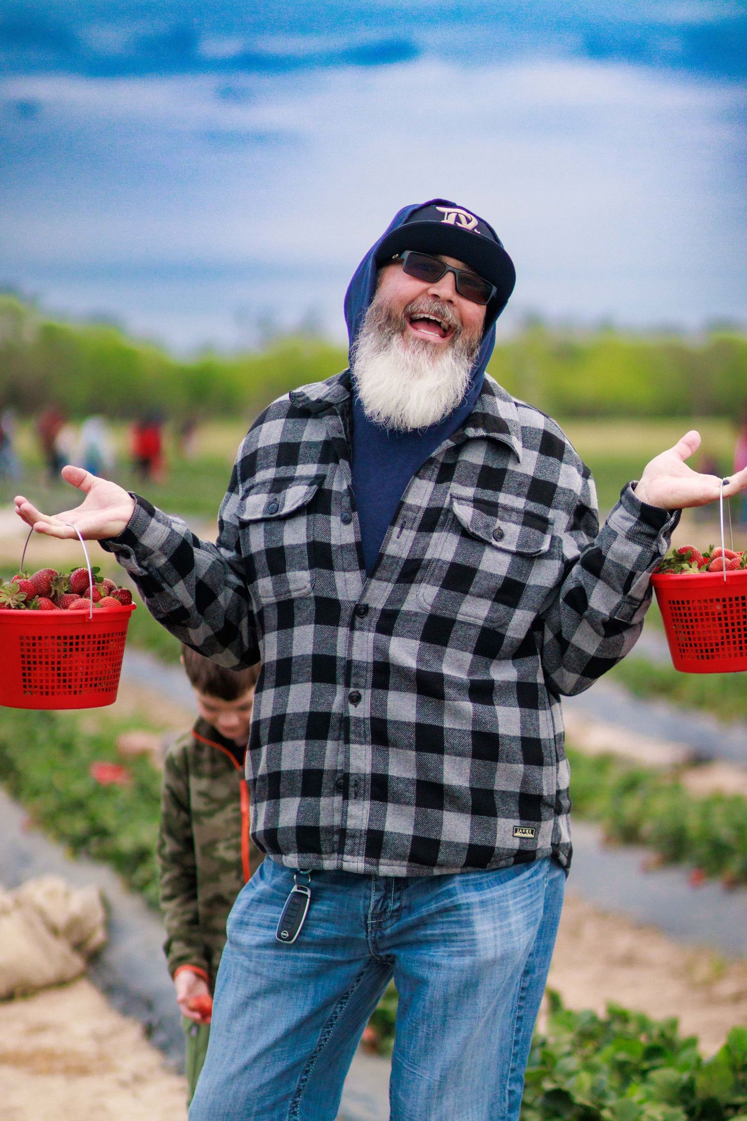 Cheerful bearded man holding red baskets of strawberries at a farm.