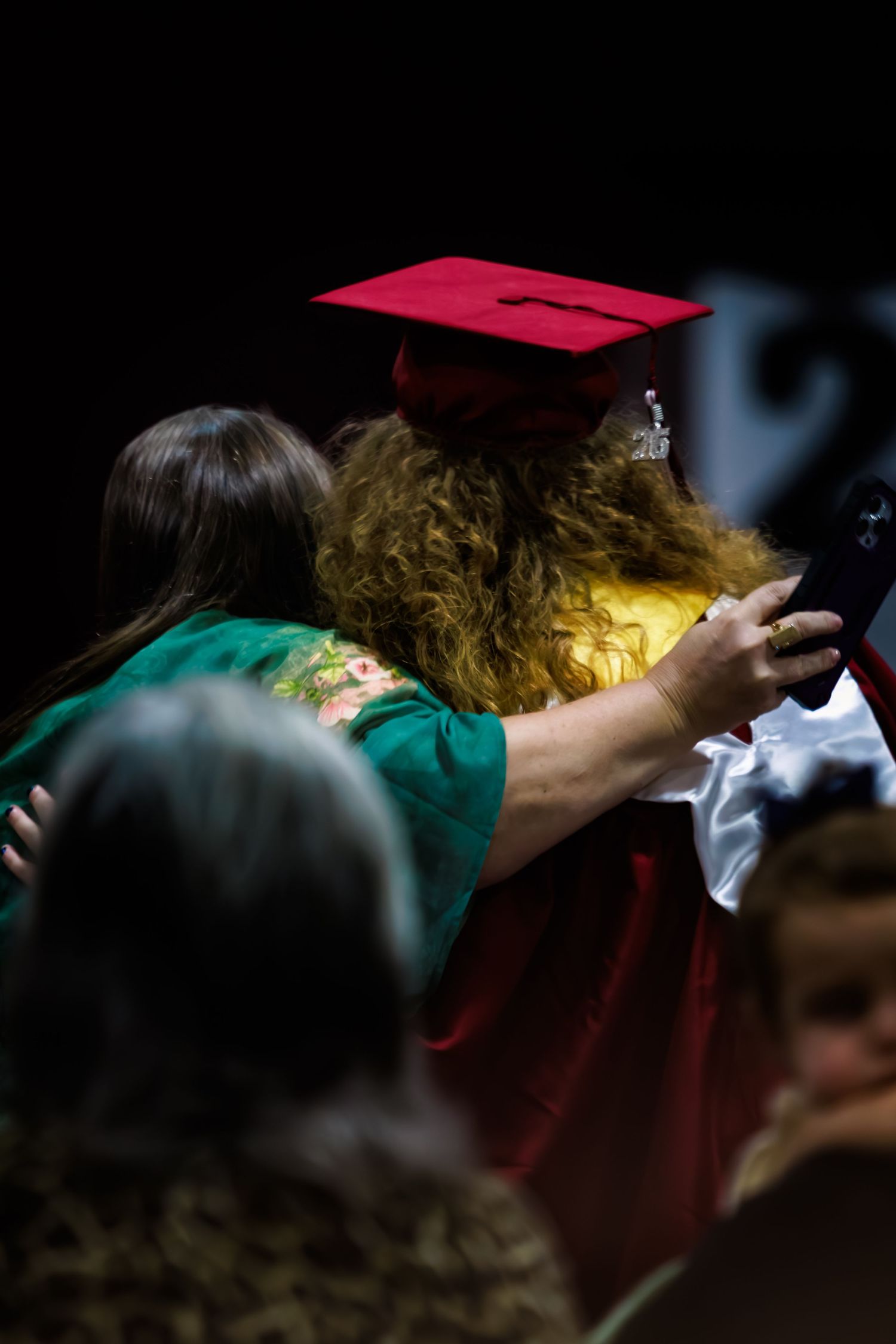 Graduate in red cap and gown shares a warm hug during graduation ceremony.