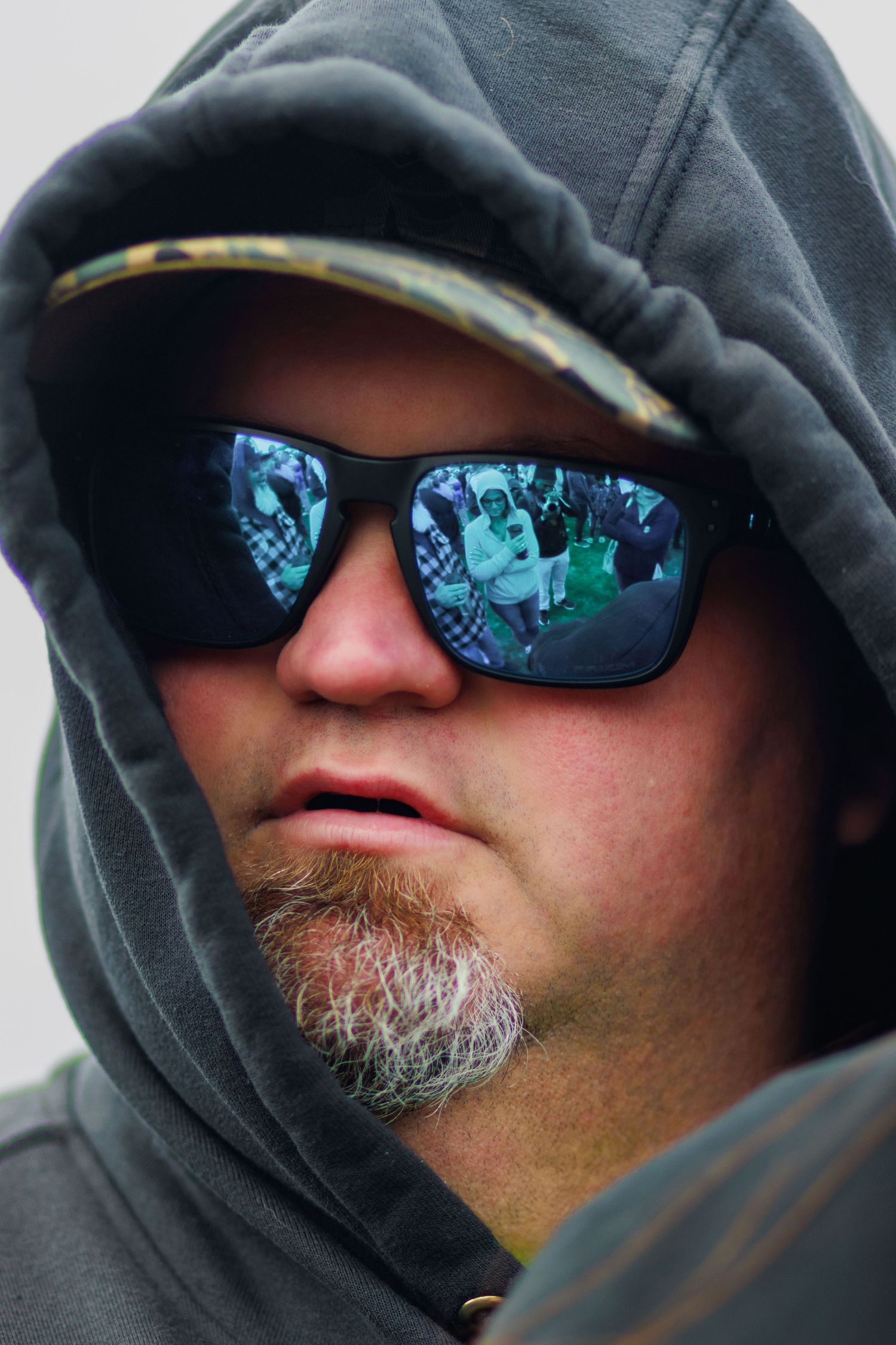 Man in gray hoodie wearing reflective blue sunglasses outdoors.