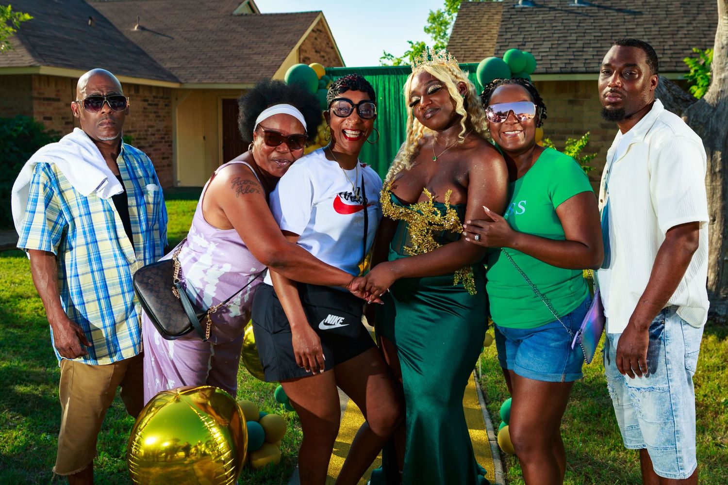 Group of friends posing together outdoors at a backyard gathering, wearing colorful outfits and holding gold balloons.