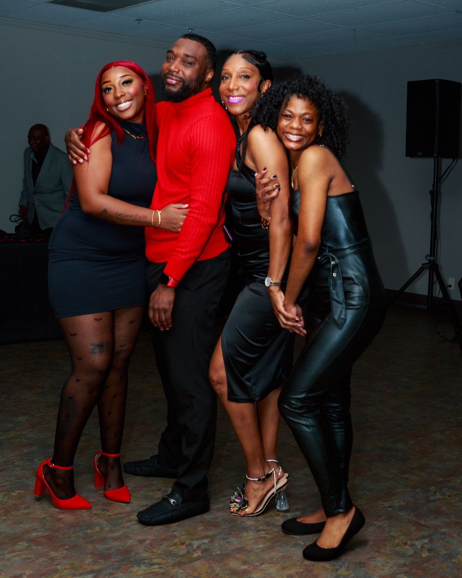 Four friends posing together at a party, dressed in elegant black and red outfits, smiling joyfully on a dance floor.