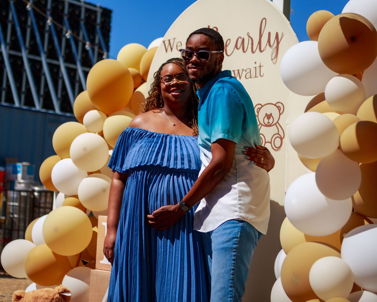 Couple posing at a baby shower in front of balloon arch display.