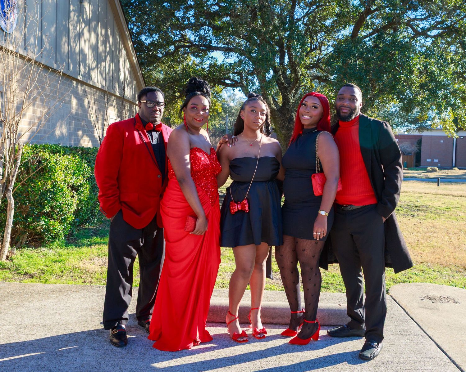 Group of five friends dressed in red and black formal attire posing together outdoors.