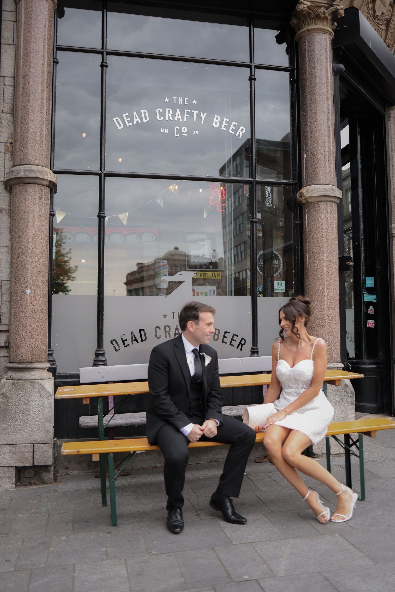 Bride and groom sitting on a bench outside Dead Crafty Beer Co. in Liverpool, sharing a romantic moment. Ruby Salmon Photography