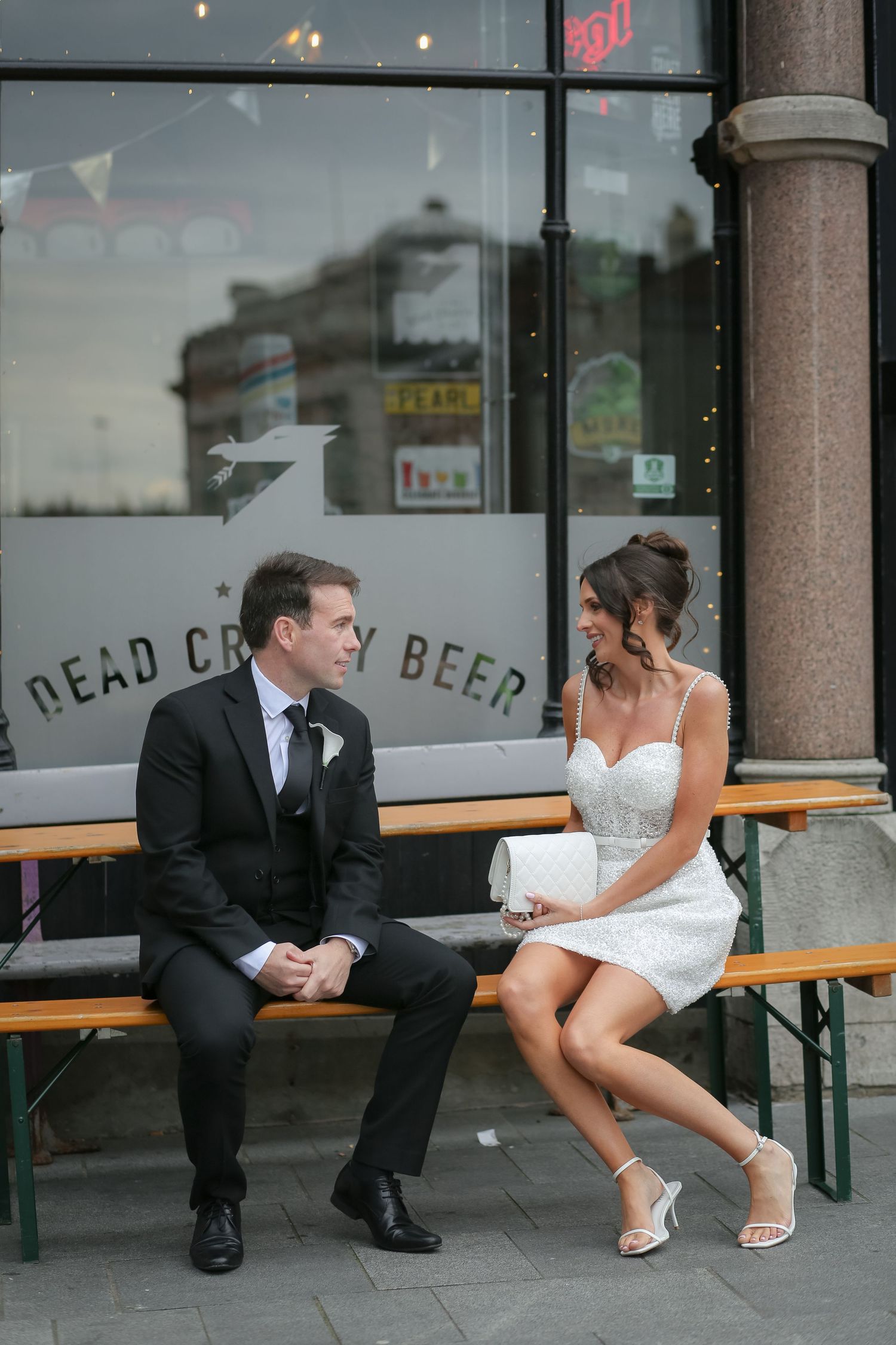 Bride and groom sitting on a bench outside Dead Craft Beer bar, sharing a romantic moment. Liverpool wedding photographer, Ruby Salmon Photo