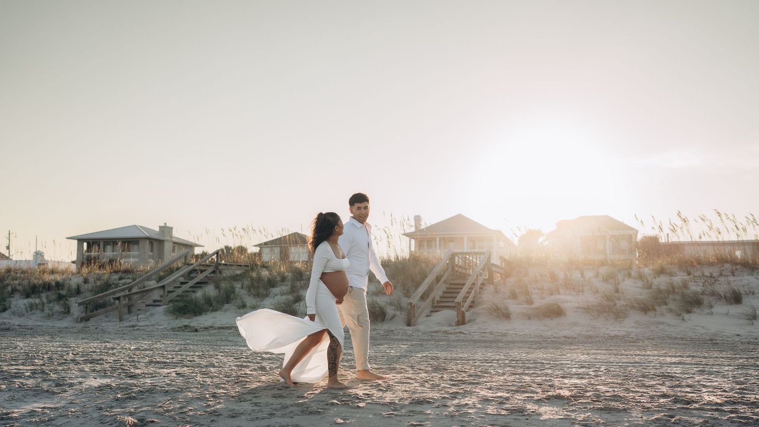 Panoramic beach sunset scene with coastal homes and figures walking in the distance.