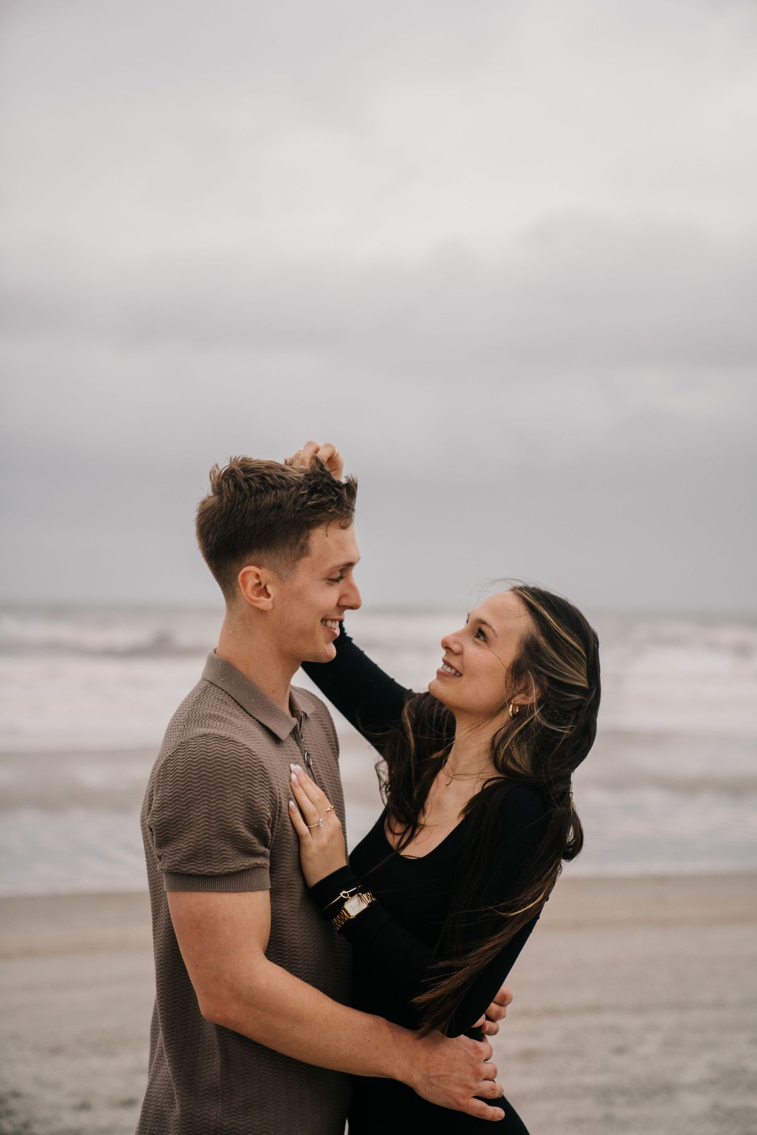 Romantic couple sharing intimate moments on a cloudy beach with waves crashing in the background.