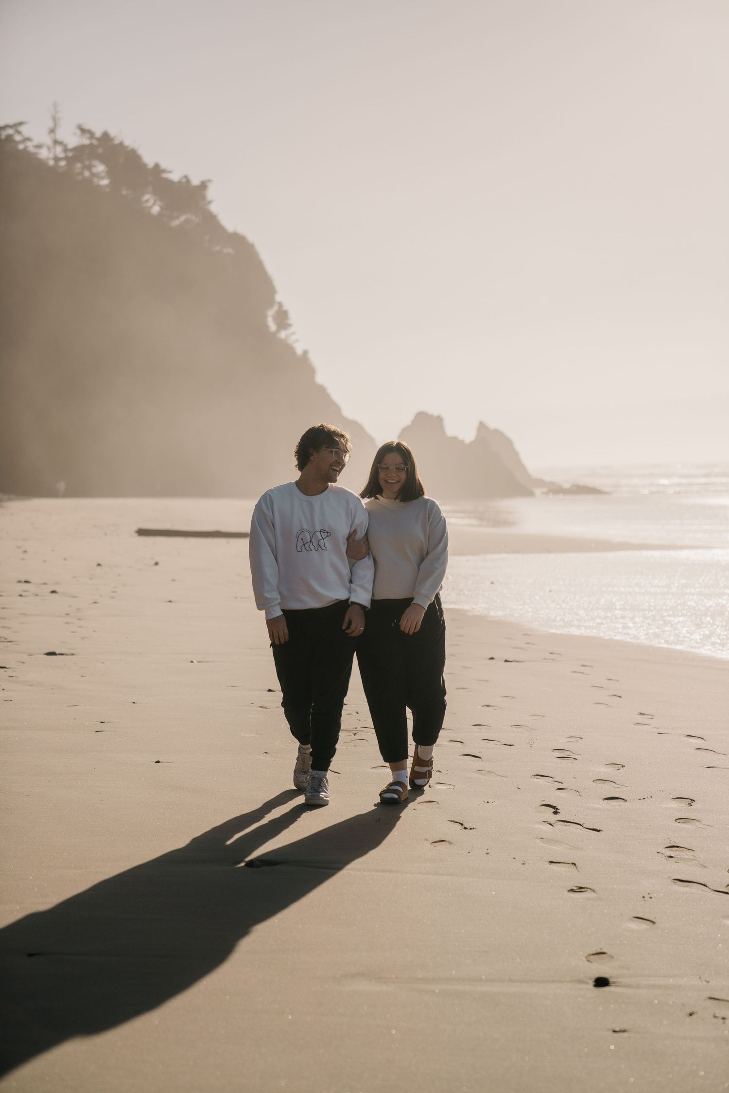 Long shadows cast by a couple walking on a misty beach at sunset.