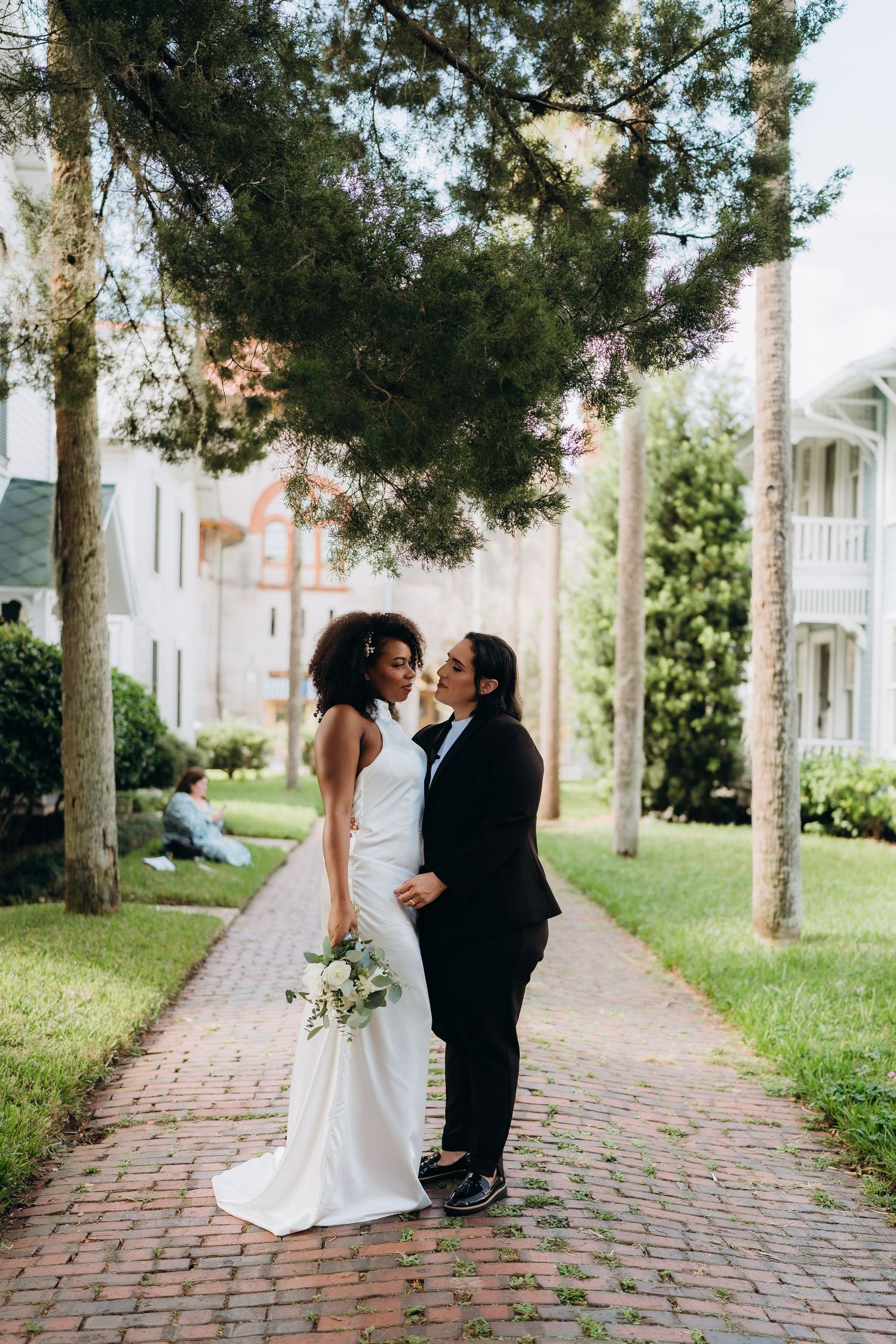A couple shares an intimate moment on a brick path lined with palm trees and historic buildings.