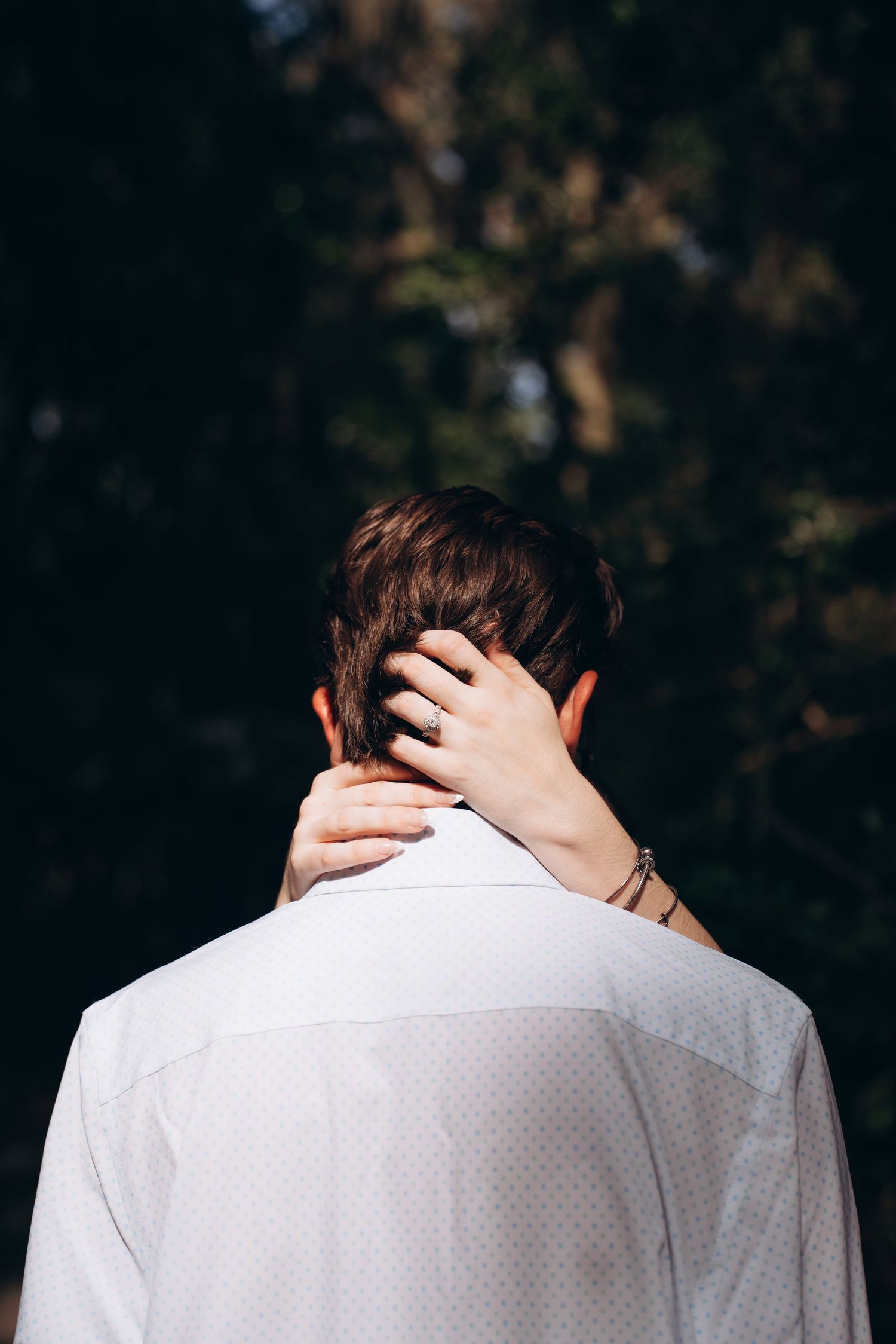 A person in a white dress shirt is photographed from behind with a hand on their neck.