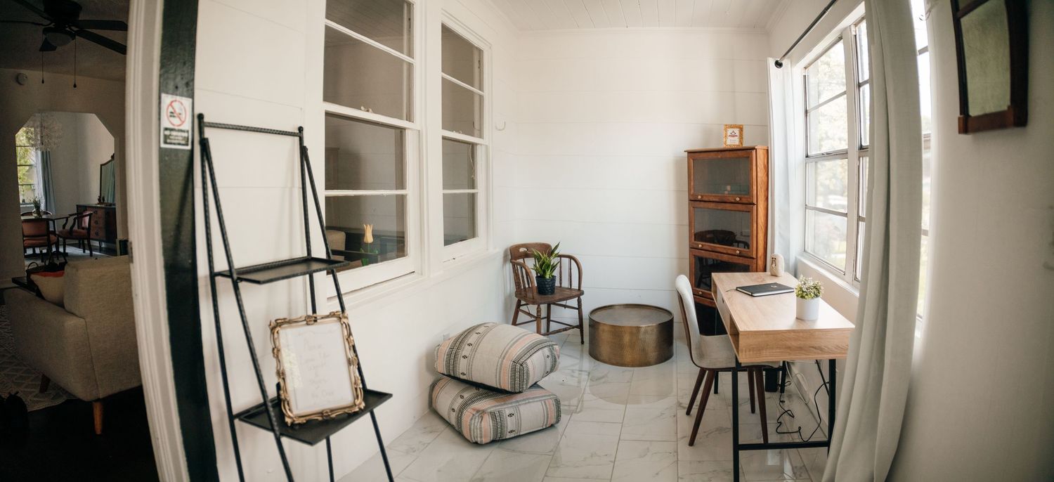 Bright minimalist room with ladder shelf, wooden furniture, cushions, and large windows.