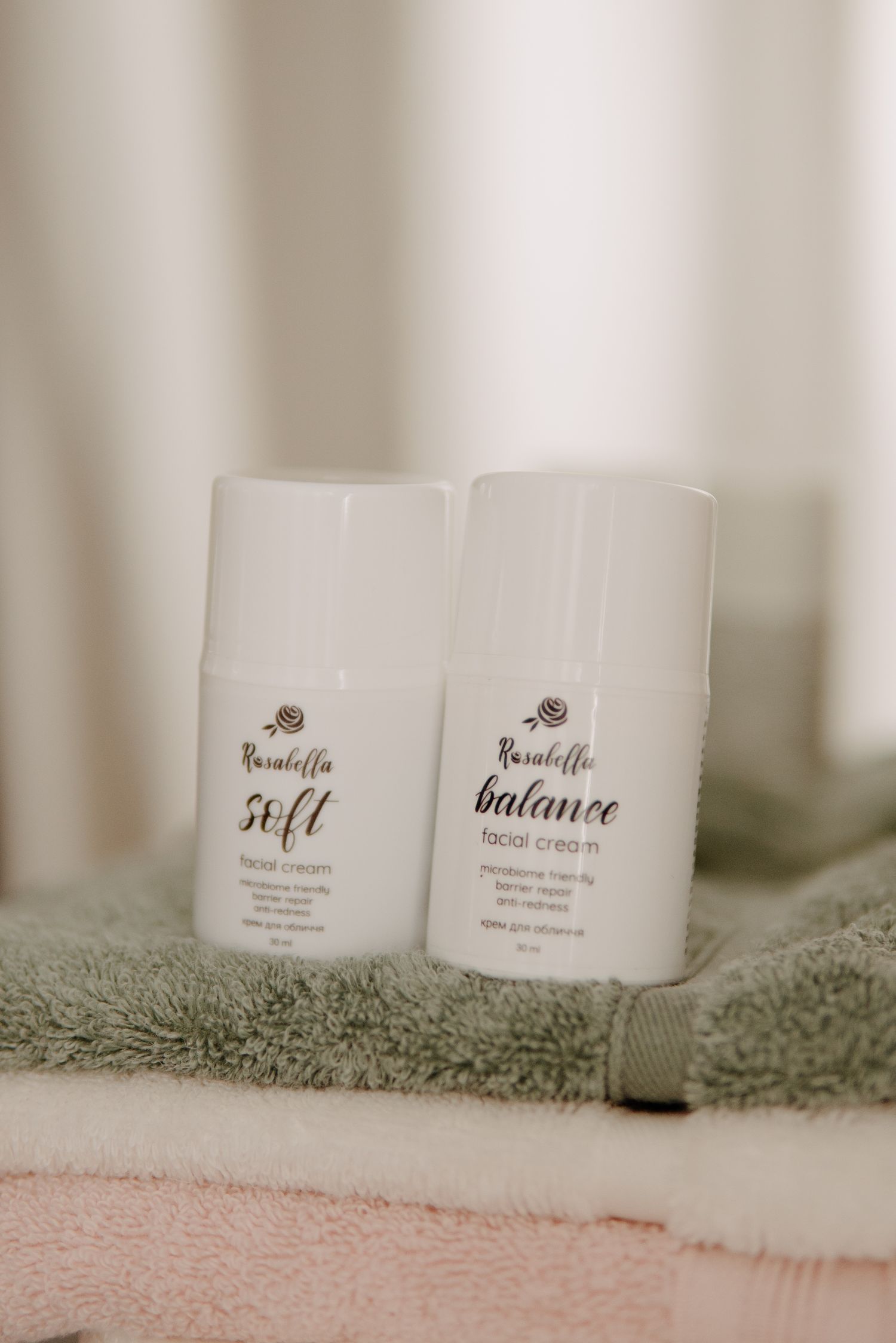 Two Rasabella soft and balance facial cream bottles placed on folded gray and pink towels.