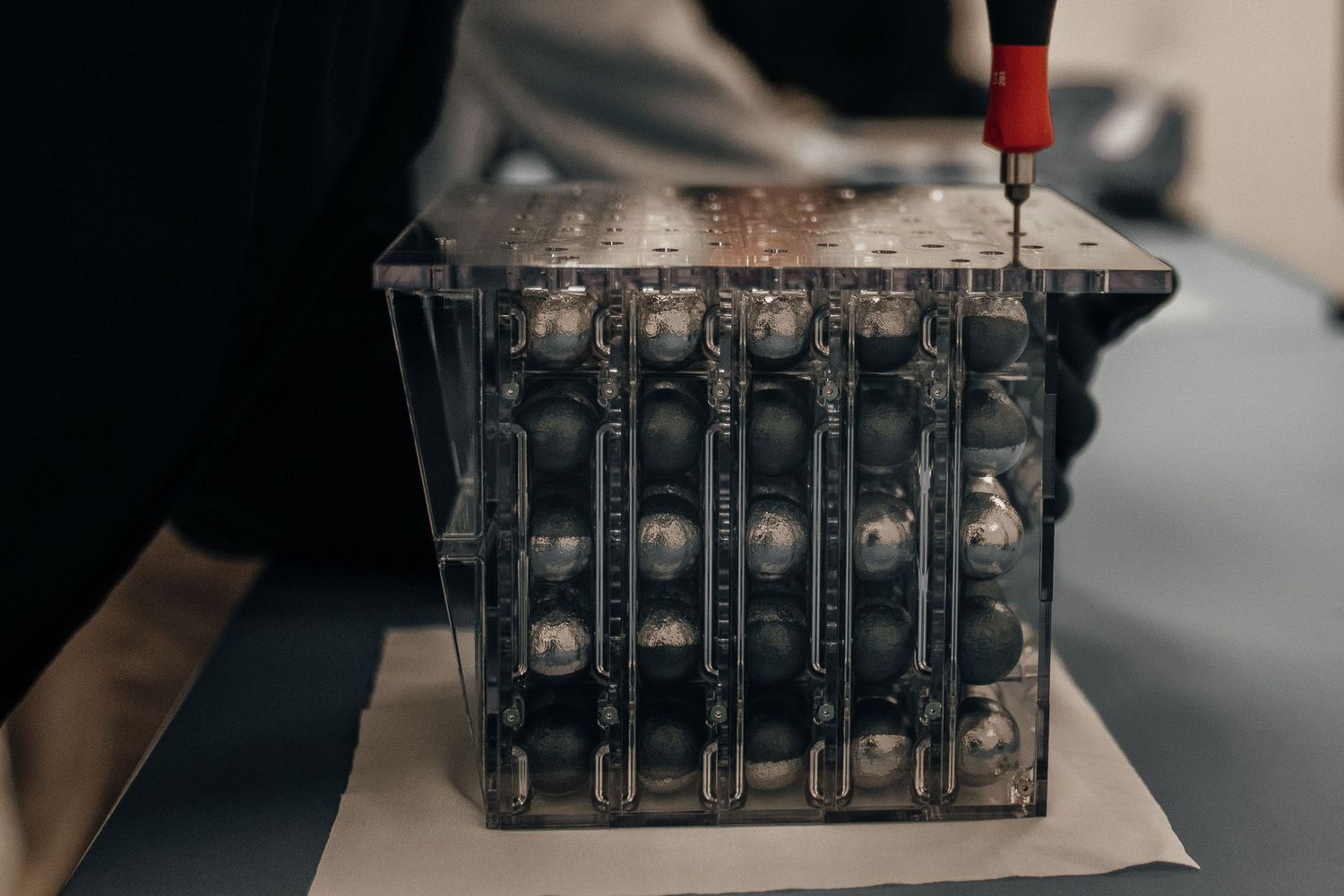 Close-up of a black cylindrical battery cell module being assembled with a screwdriver in a manufacturing setting.