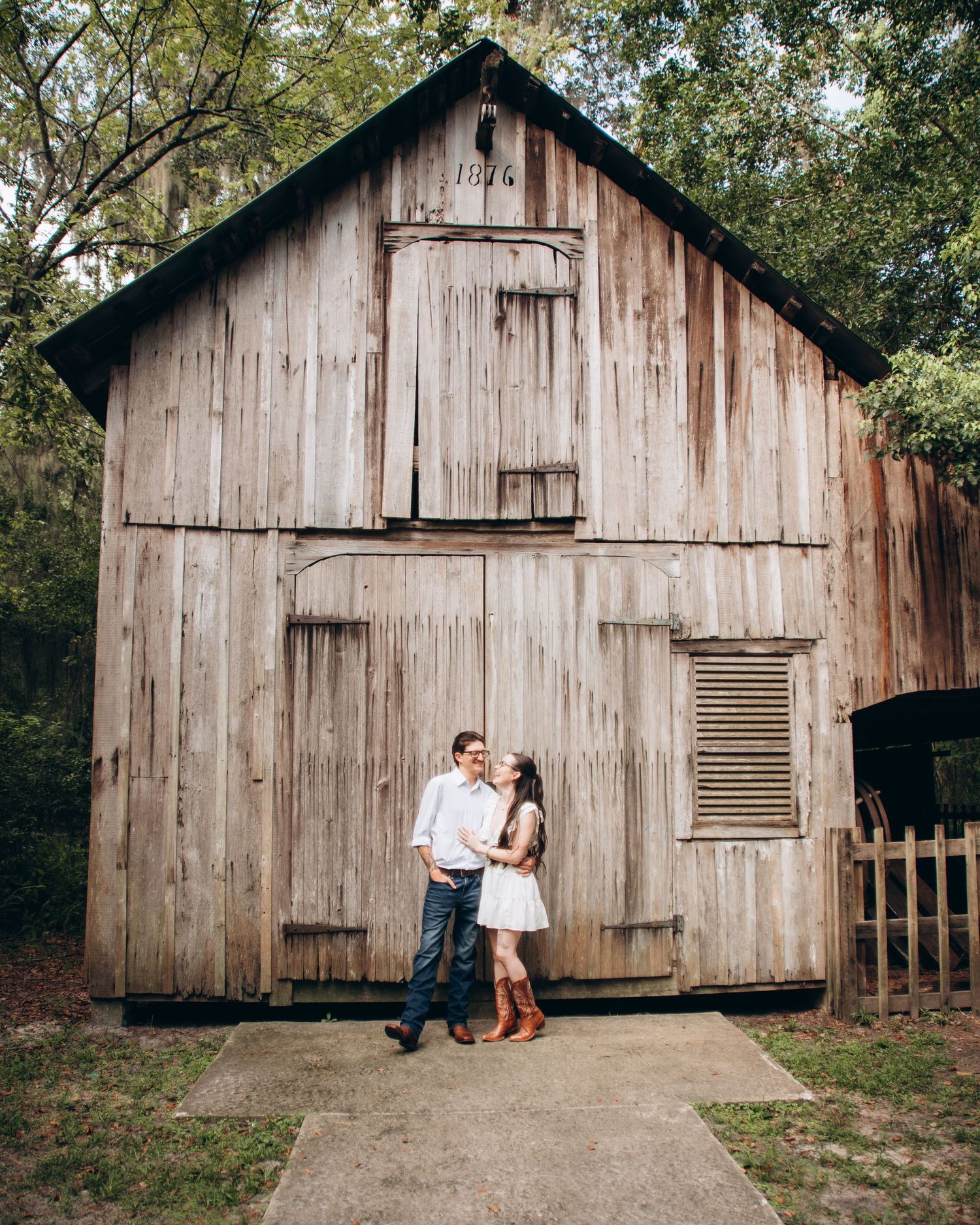 A rustic wooden barn serves as a backdrop for a romantic photoshoot in a natural outdoor setting.