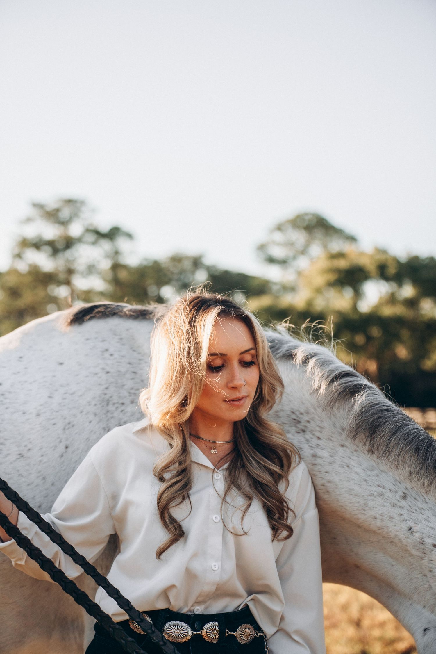 Artistic portrait in golden light featuring a white horse and western-style outfit with decorative belt.