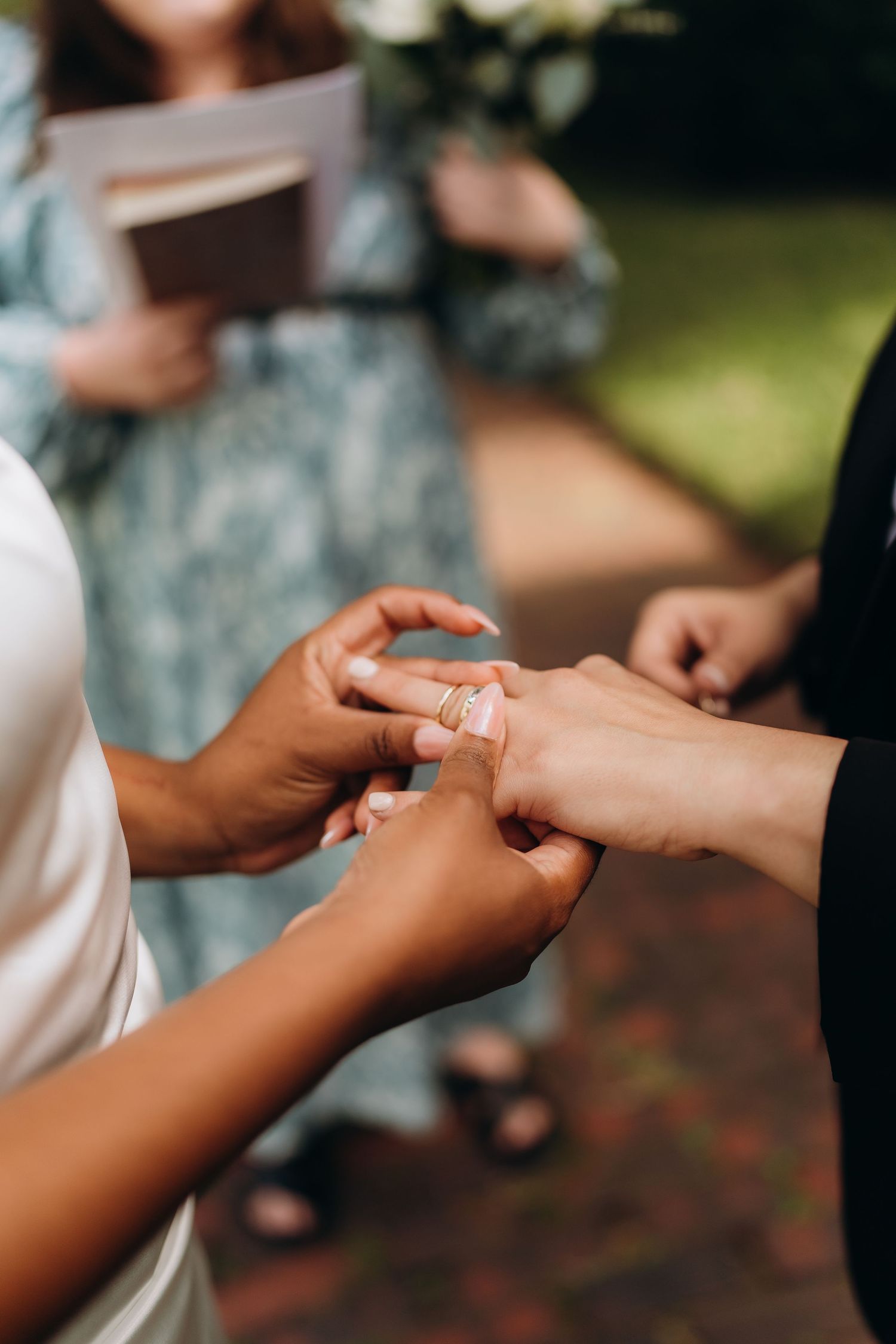 Close-up of hands exchanging wedding rings during an outdoor ceremony.