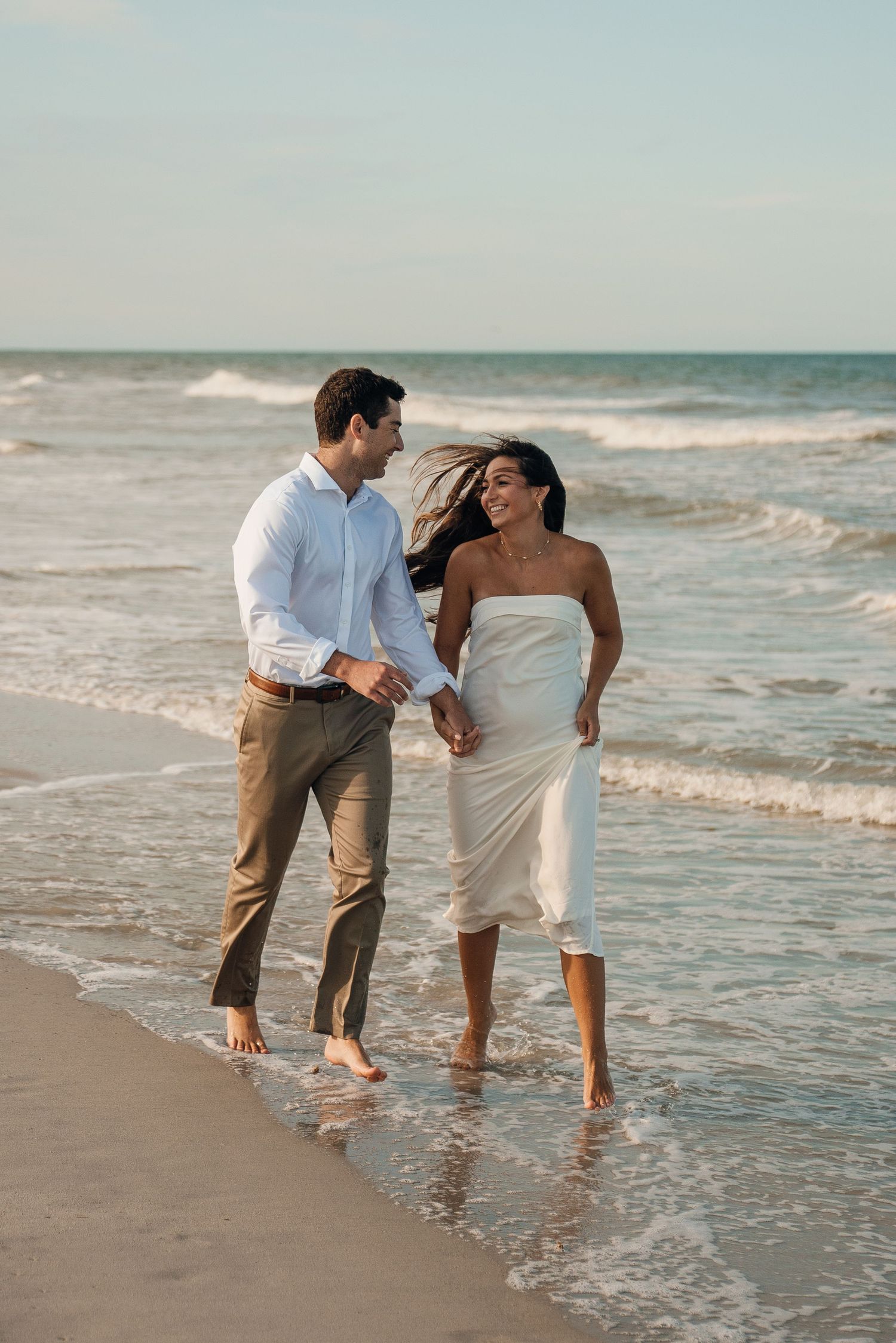 A playful couple splashes in the ocean waves during a beach photoshoot.