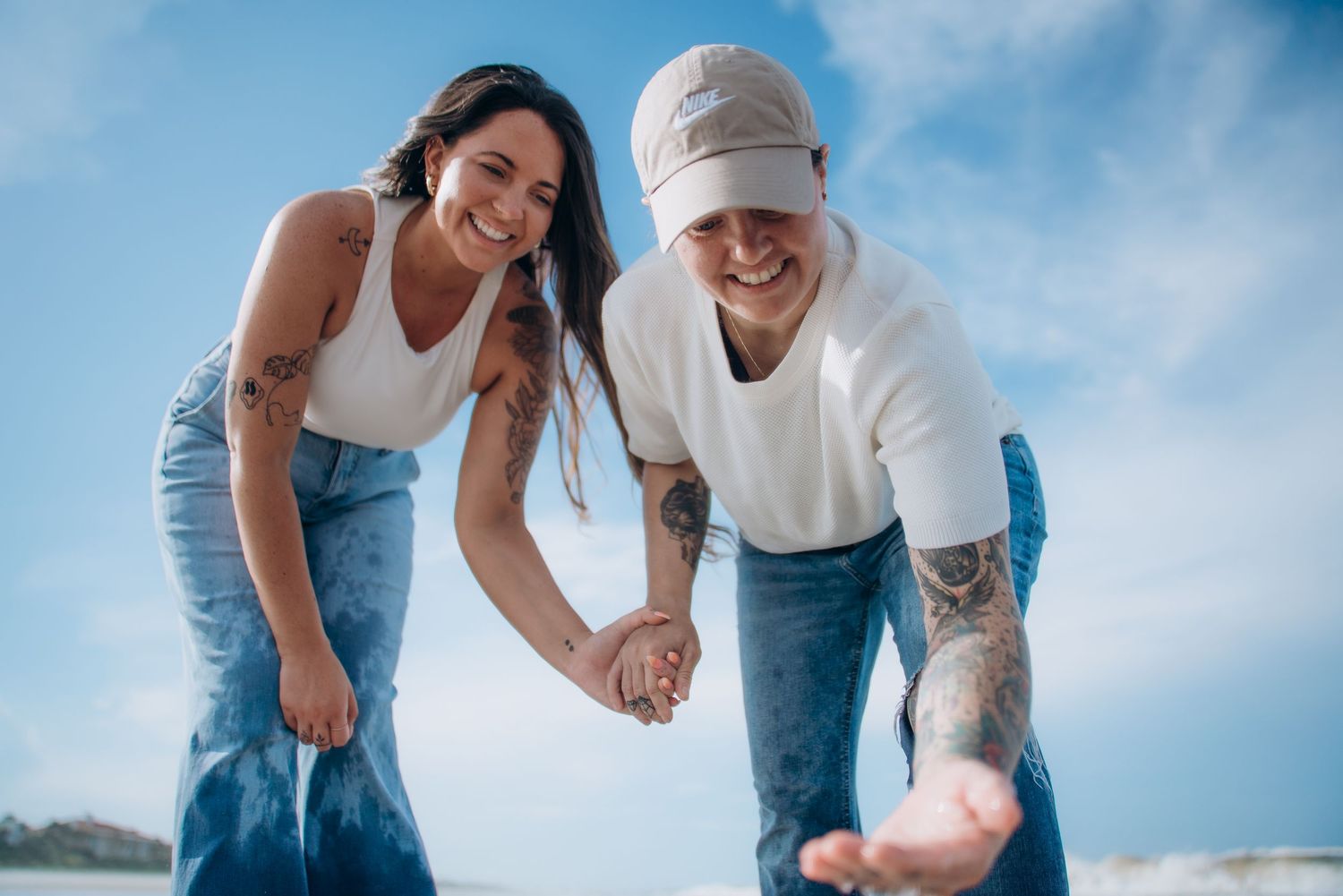 A couple holding hands and laughing together on a sunny day with blue skies in the background.