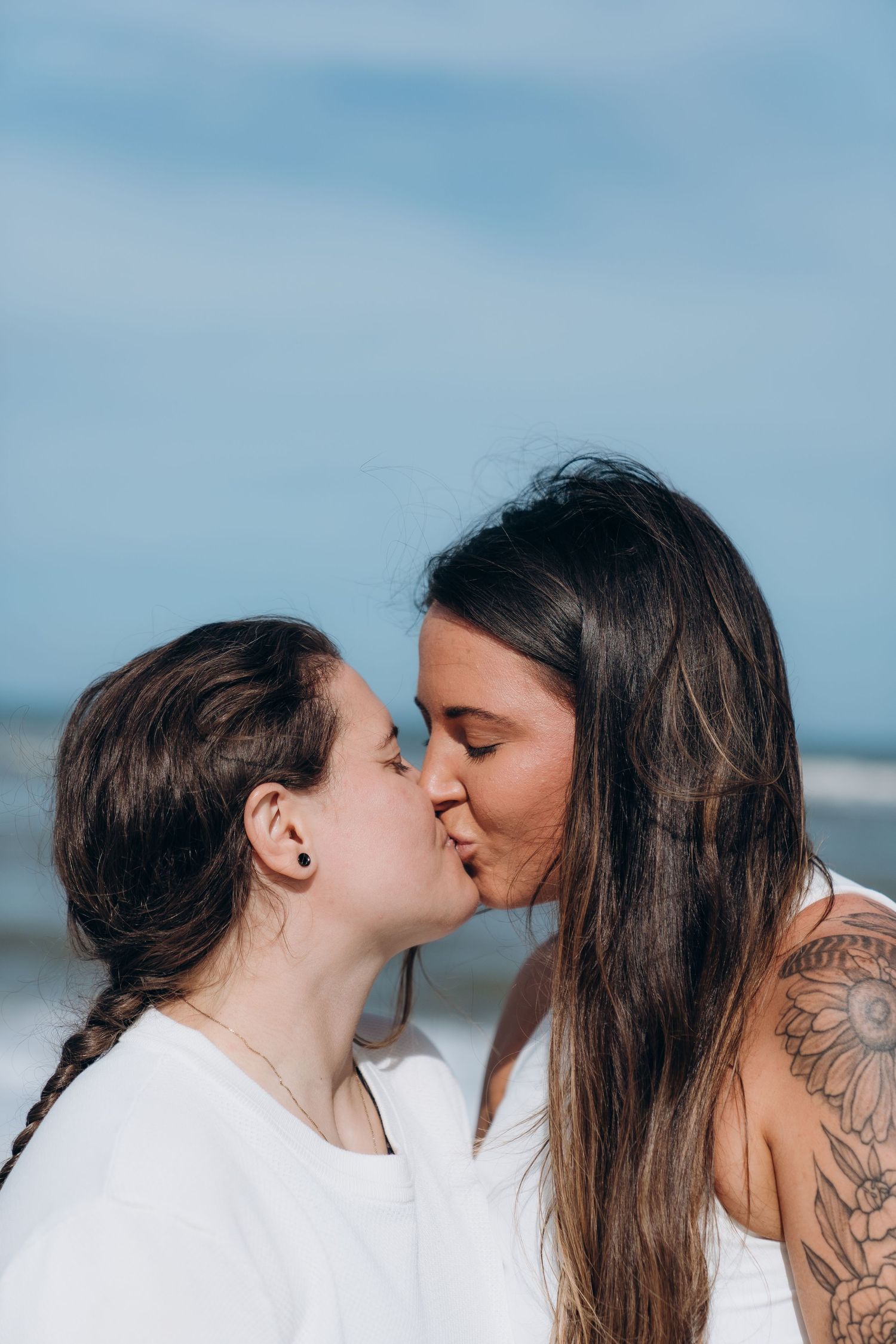 A tender moment captured between two people against a bright blue sky at the beach.
