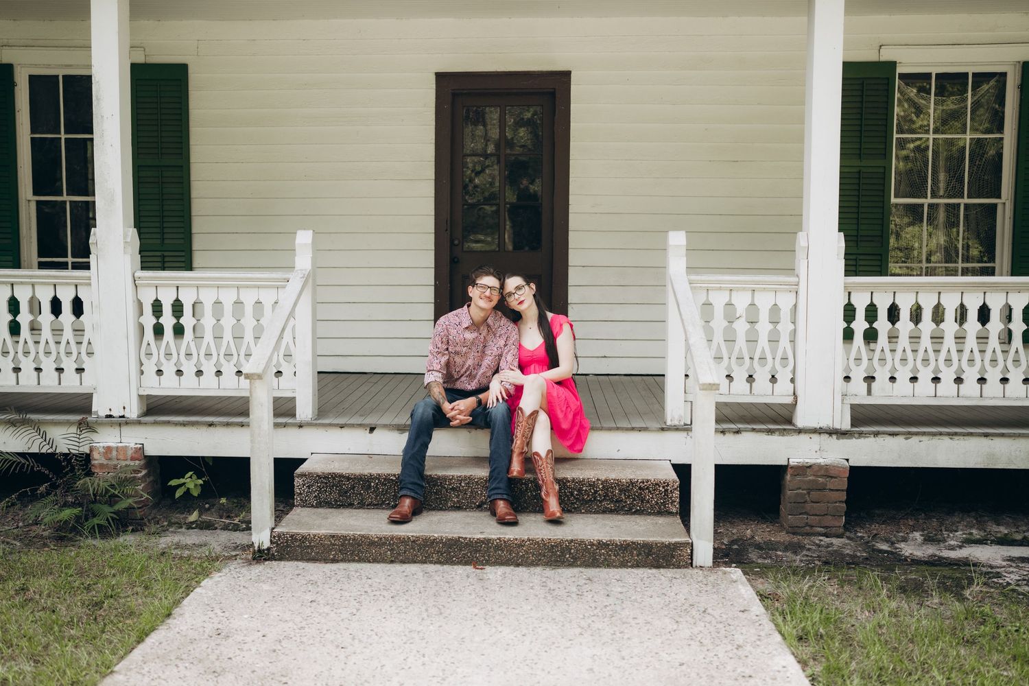 White farmhouse style porch with classic columns and dark green shutters in a peaceful outdoor setting.