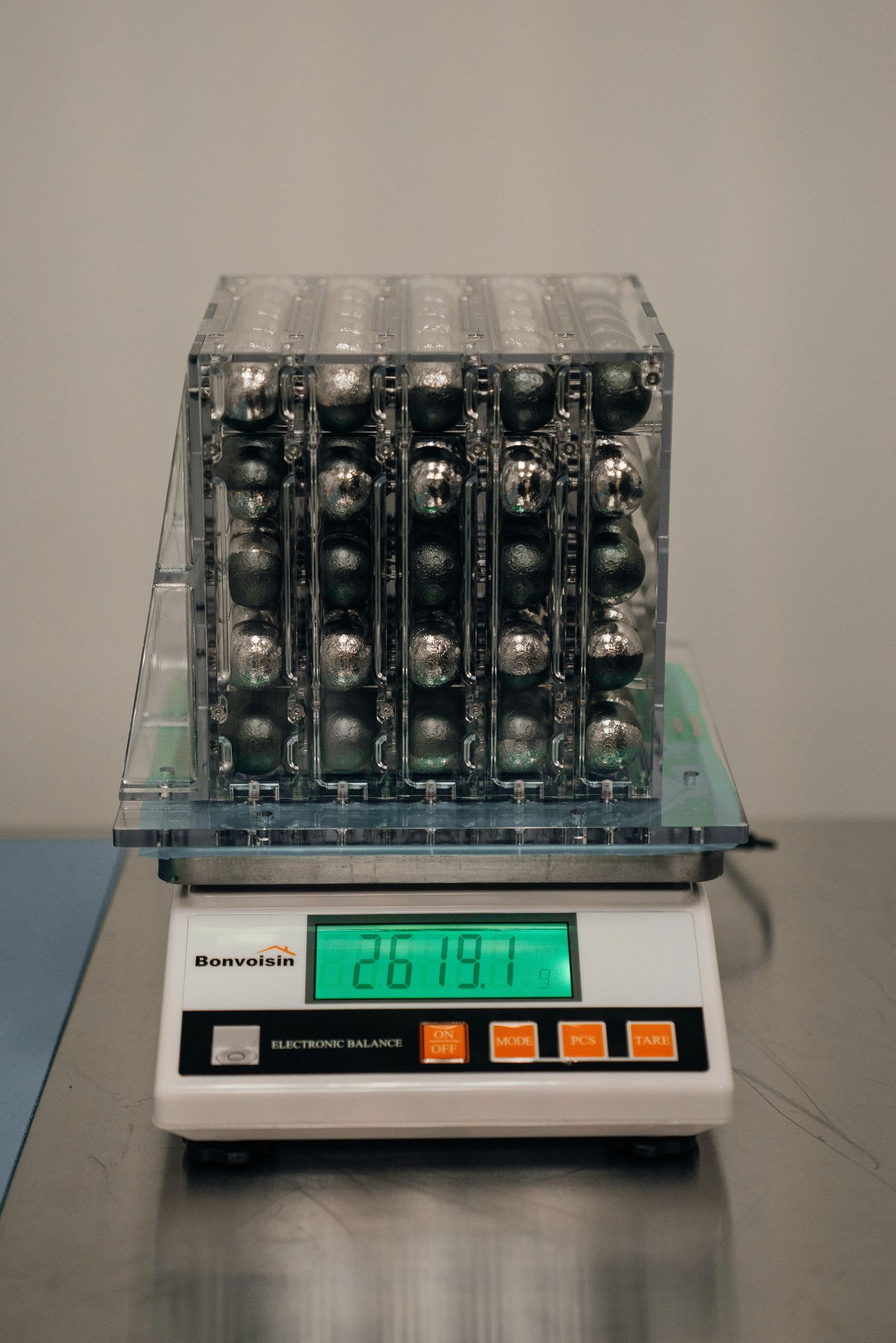 Bonvoisin electronic balance scale displaying 2613.7g with a clear container of metal balls on a stainless steel surface.