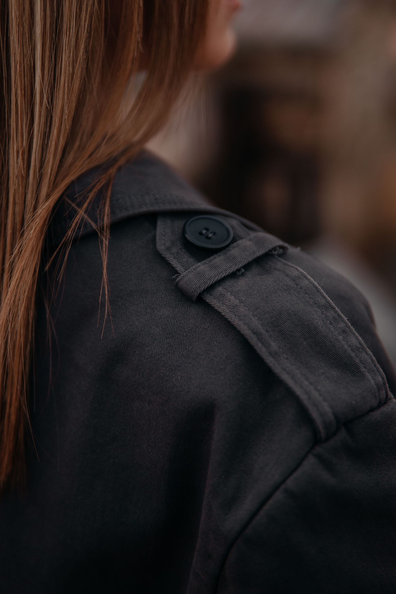 Close-up detail of dark gray jacket shoulder with decorative button epaulette on woman with auburn hair.