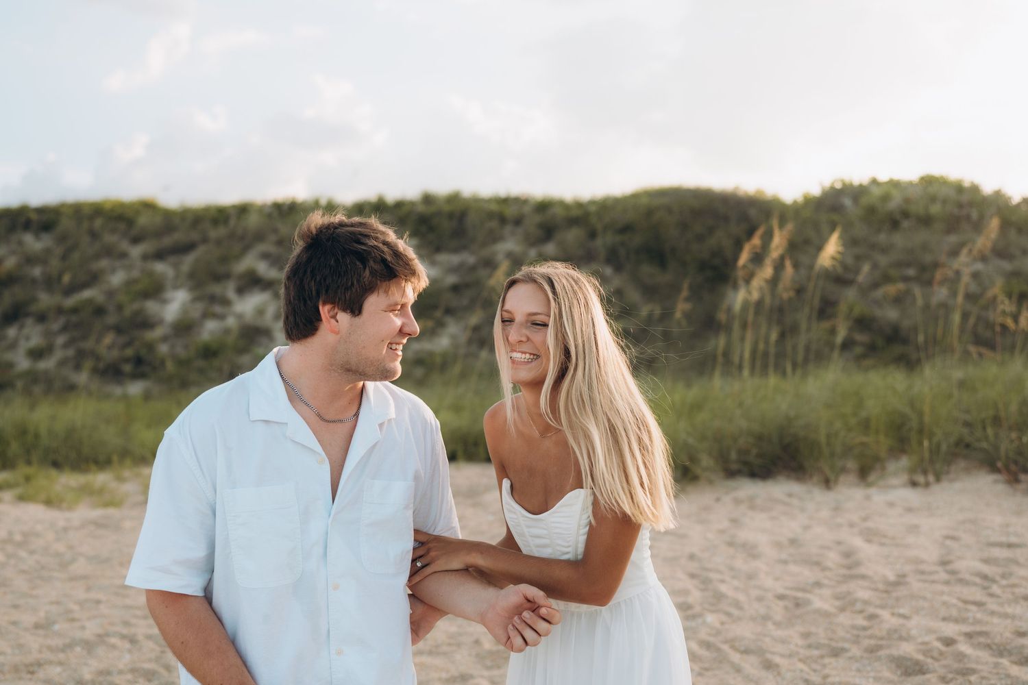 Tender moment between couple on sandy beach with coastal vegetation in background.