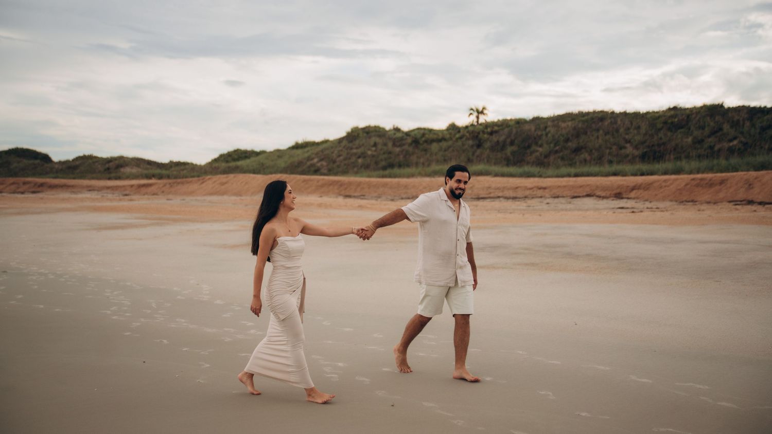 Wide angle beach landscape with couple walking along the sandy shoreline at dusk.