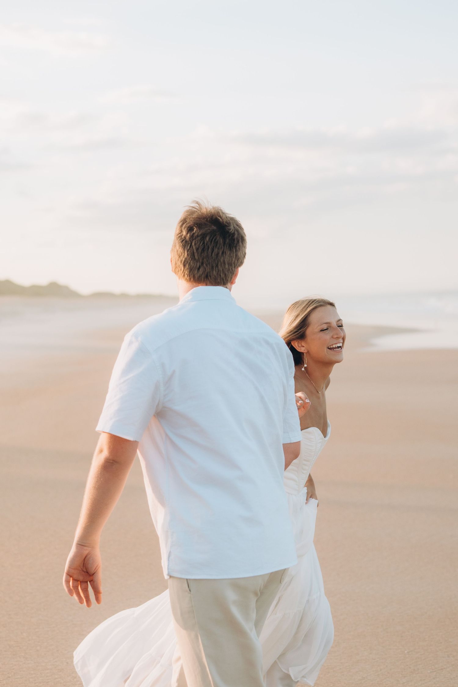 A couple runs playfully across a sandy beach during a photo session.