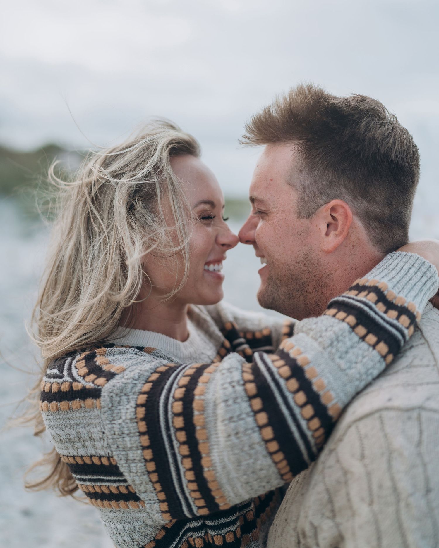 A couple wearing matching patterned sweaters share an intimate moment against a bright background.