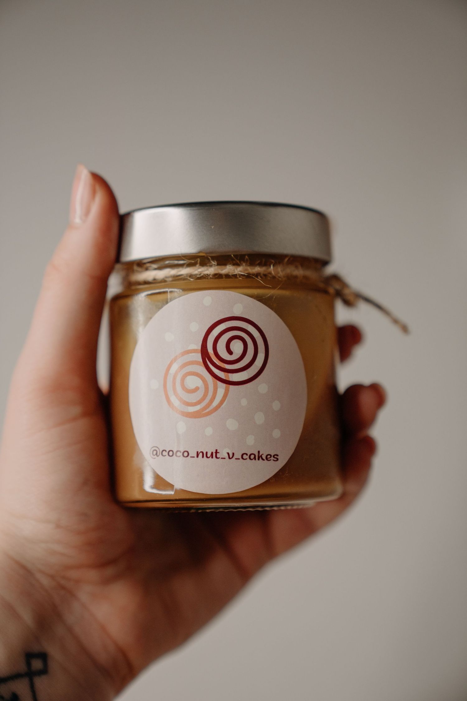 Hand holding a small jar of caramel spread with coco.nut.v.cakes branded label.